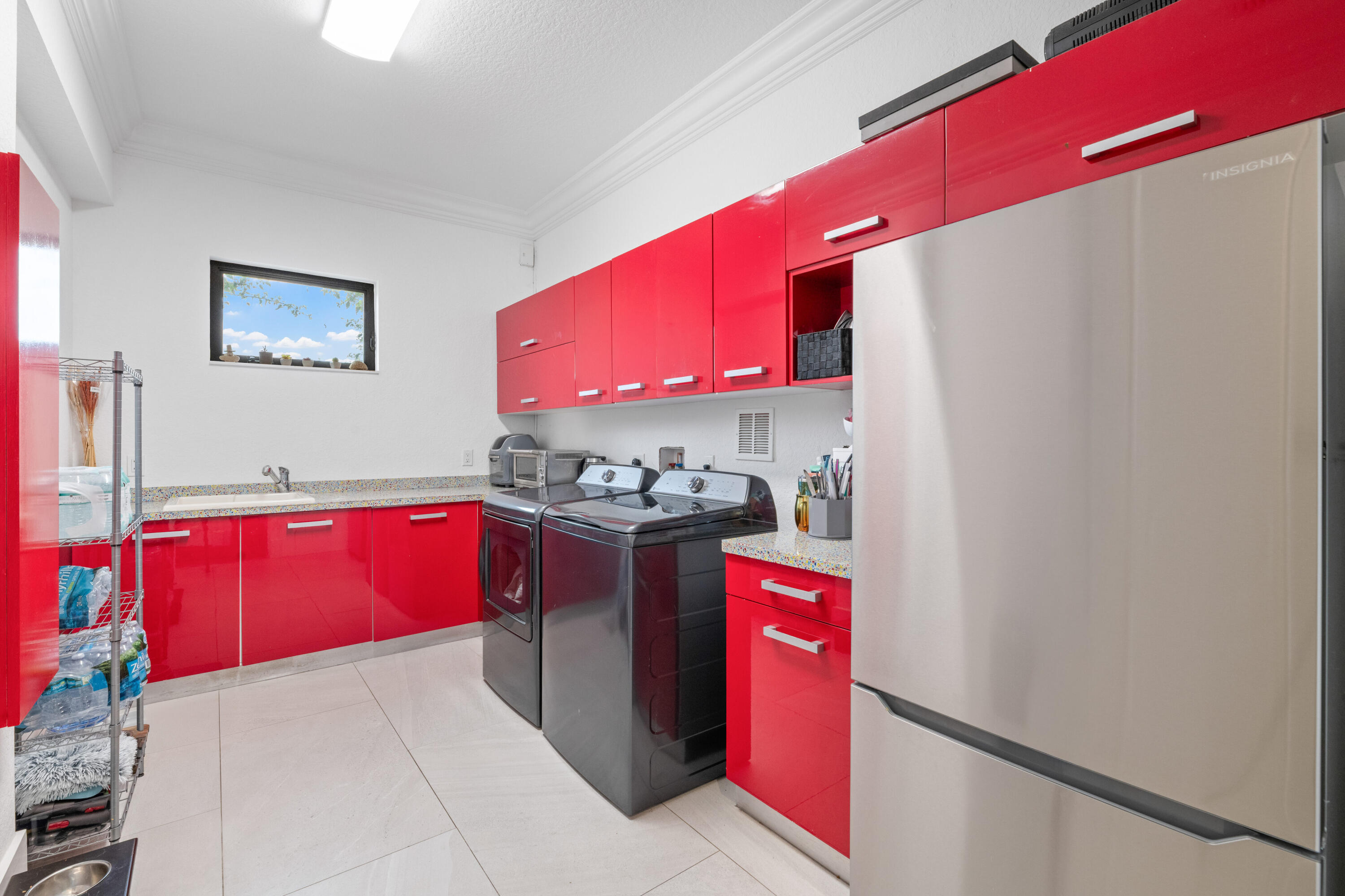 Laundry room with glossy red cabinets, washer and dryer, utility sink, and stainless-steel refrigerator.