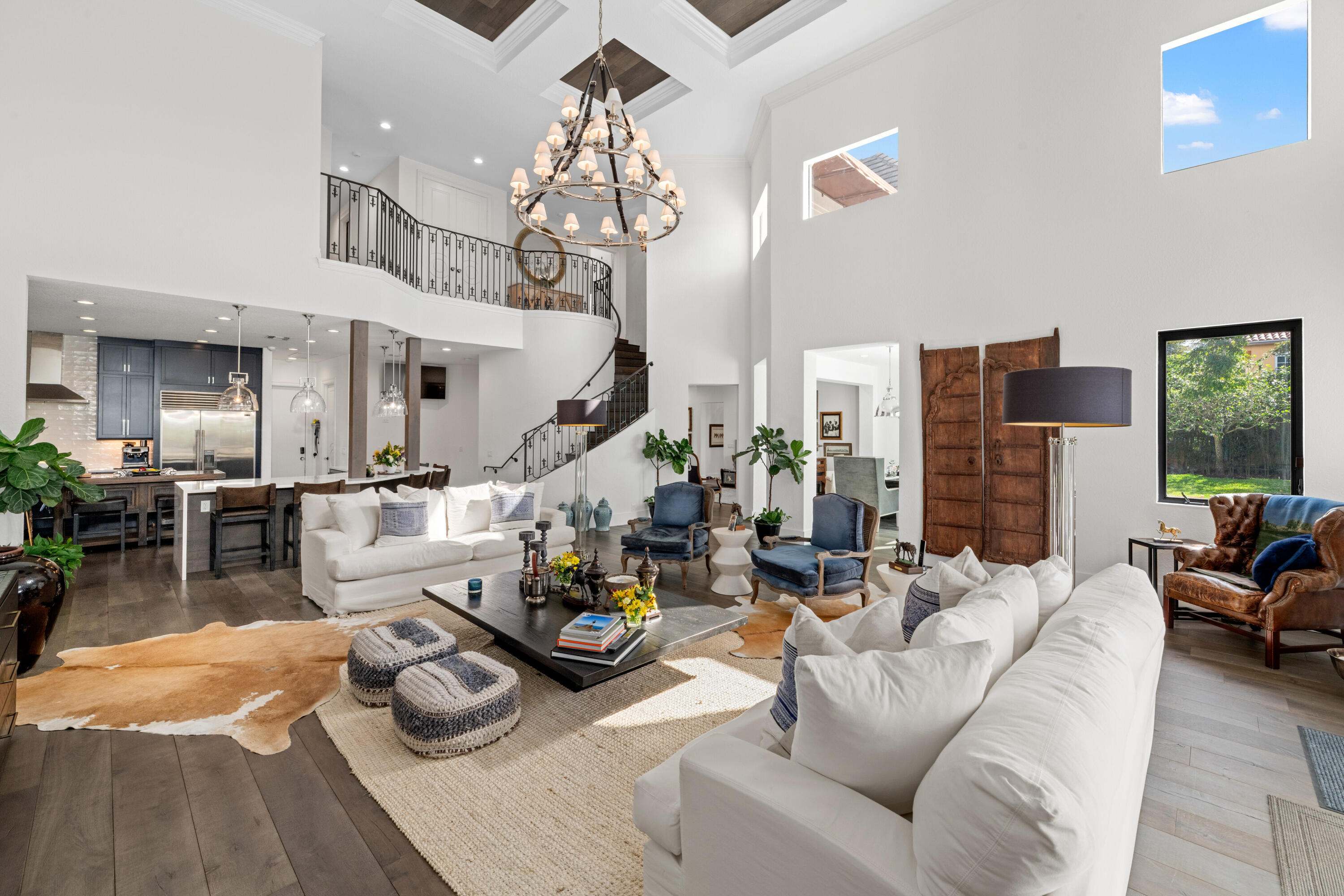Two-story living room with white sofas, blue armchairs, and a sweeping iron-railed staircase.