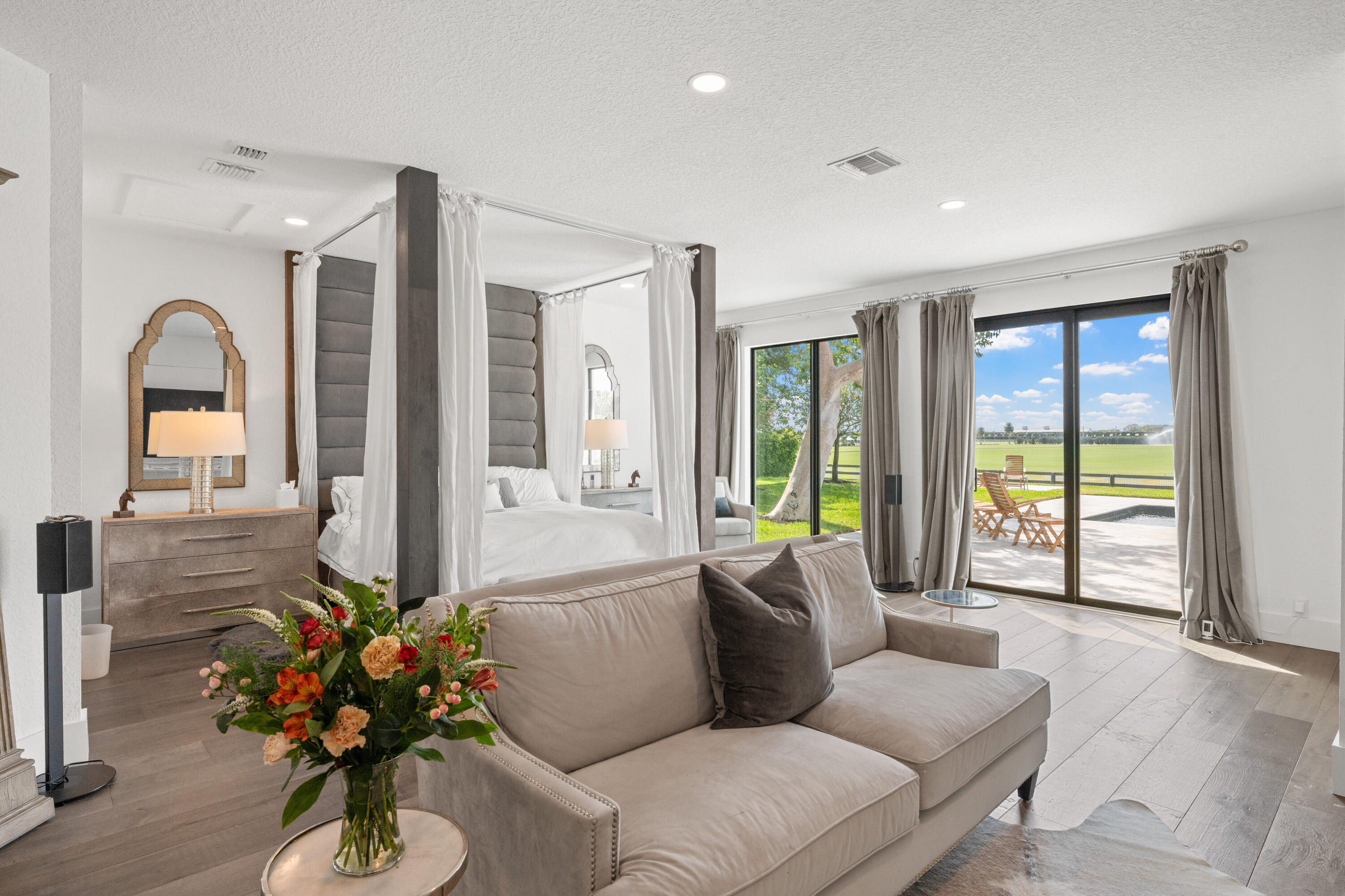 Canopy bedroom with a taupe sectional and sliding doors opening to a sunny patio and lawn.
