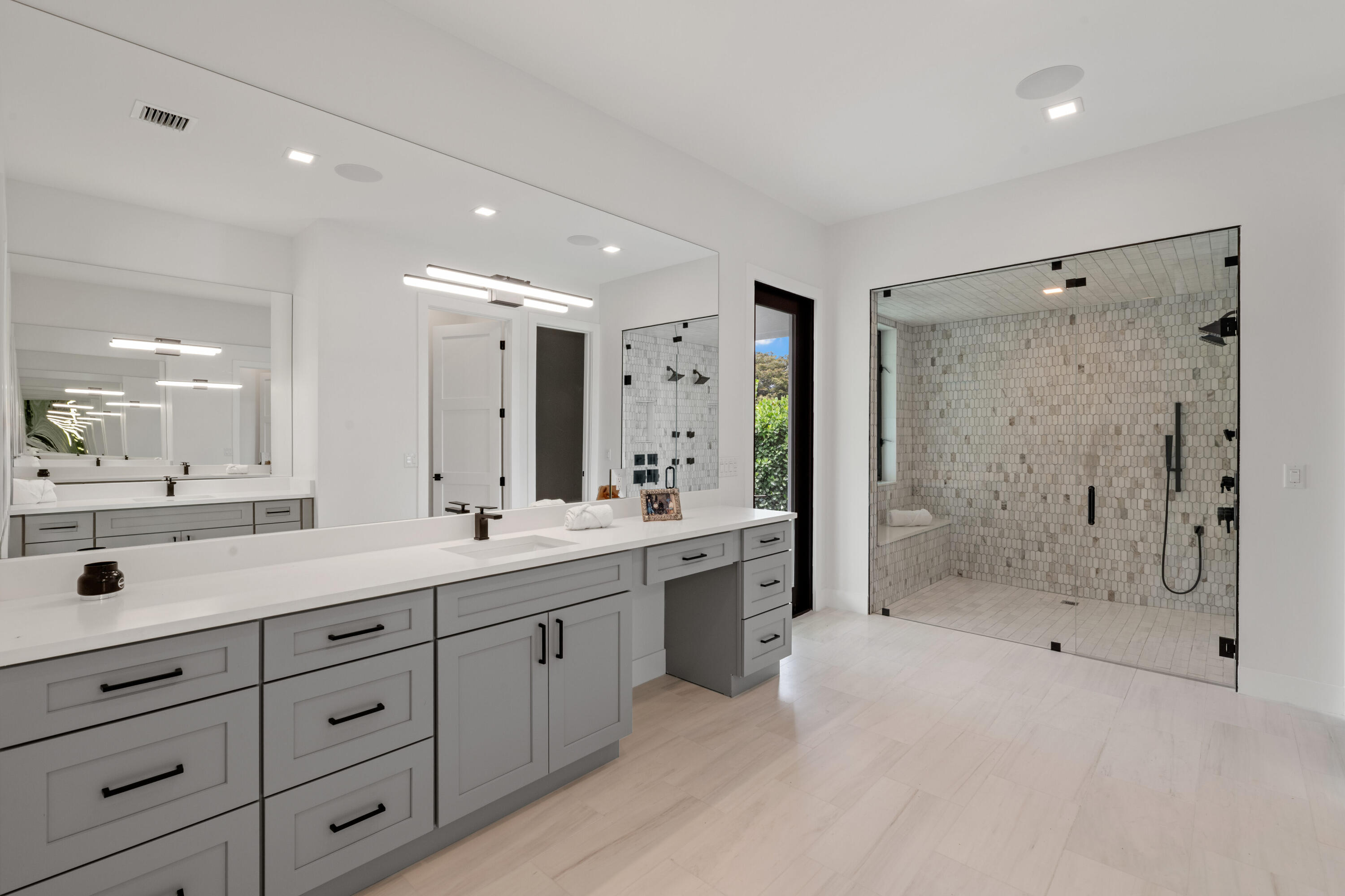 Modern bathroom with a long gray vanity and a glass-enclosed mosaic-tile shower.