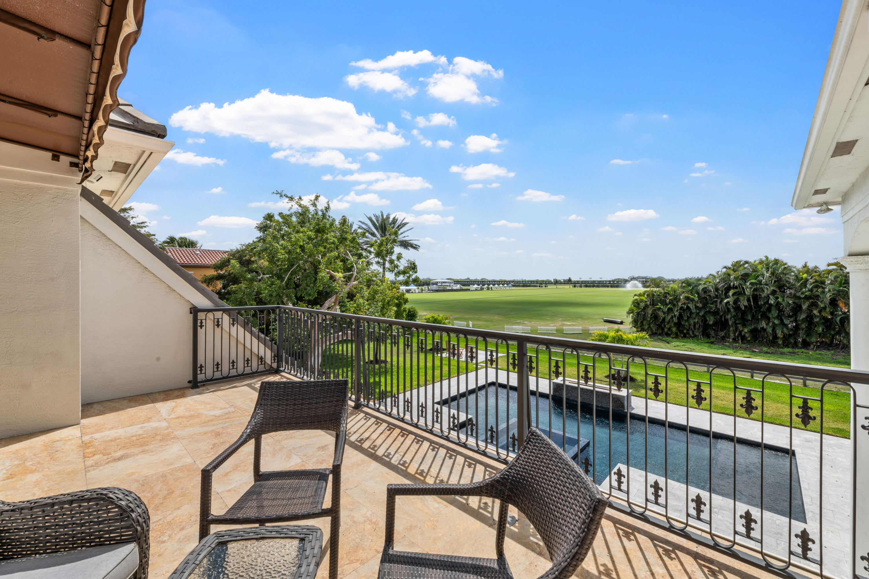 Furnished balcony overlooking a swimming pool and broad green field.