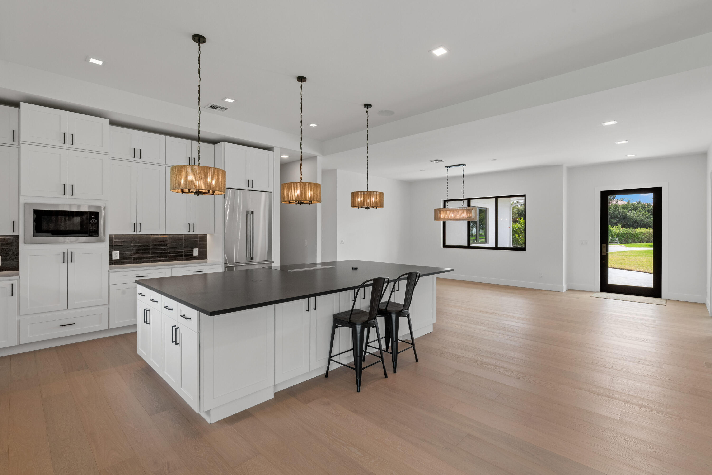 Open-plan kitchen with white cabinets, a large dark island, pendant lights, and wood flooring.