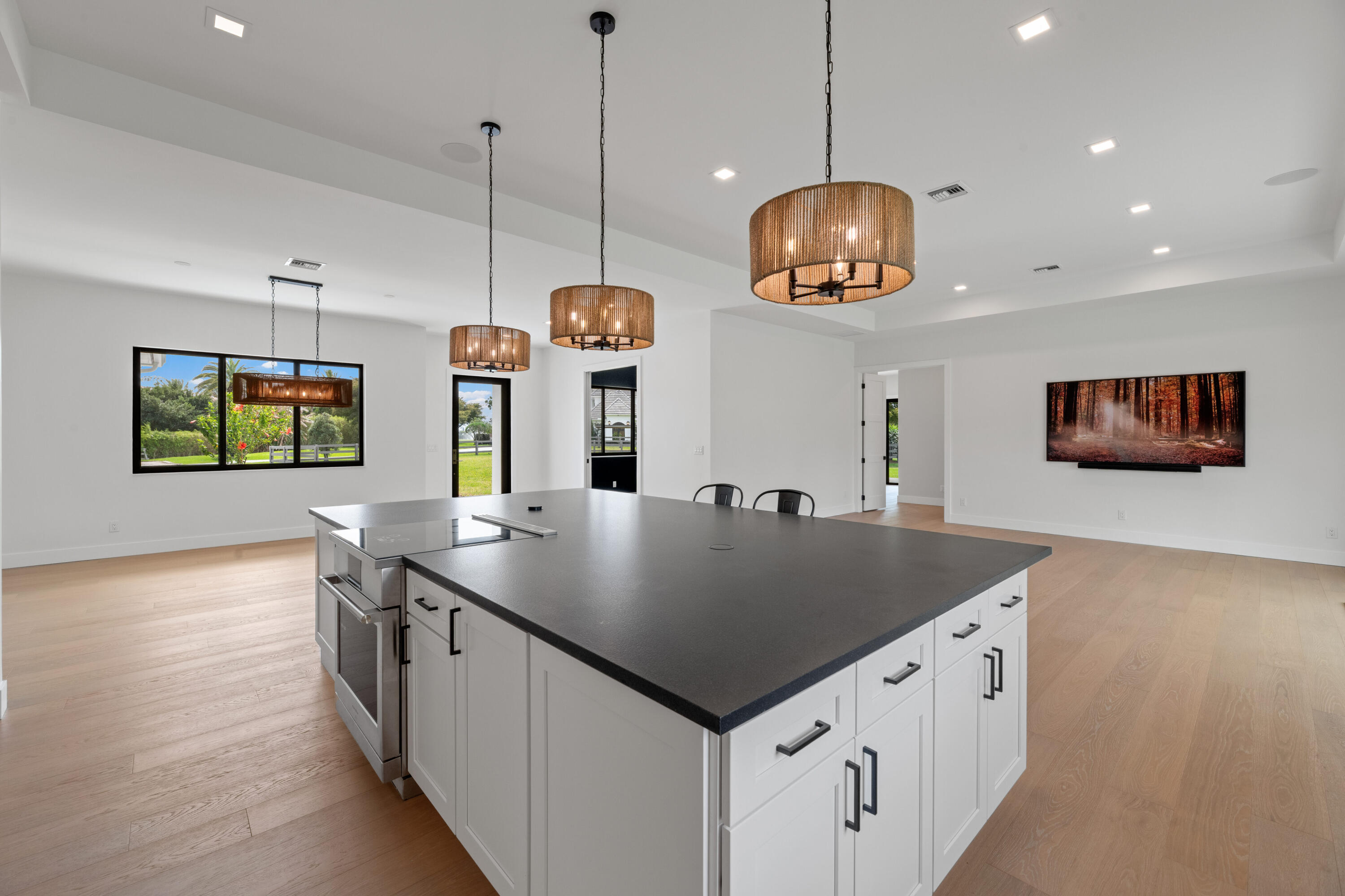 Modern kitchen with a large dark-topped island, woven pendant lights, and windows overlooking a green yard.