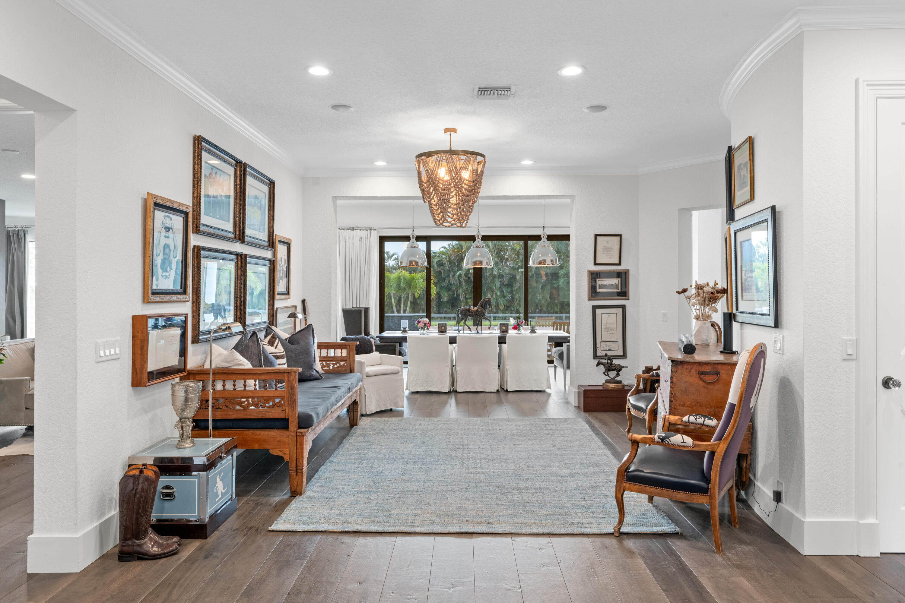 Living room with a wood-framed sofa and blue-gray rug, opening to a dining area overlooking palms.