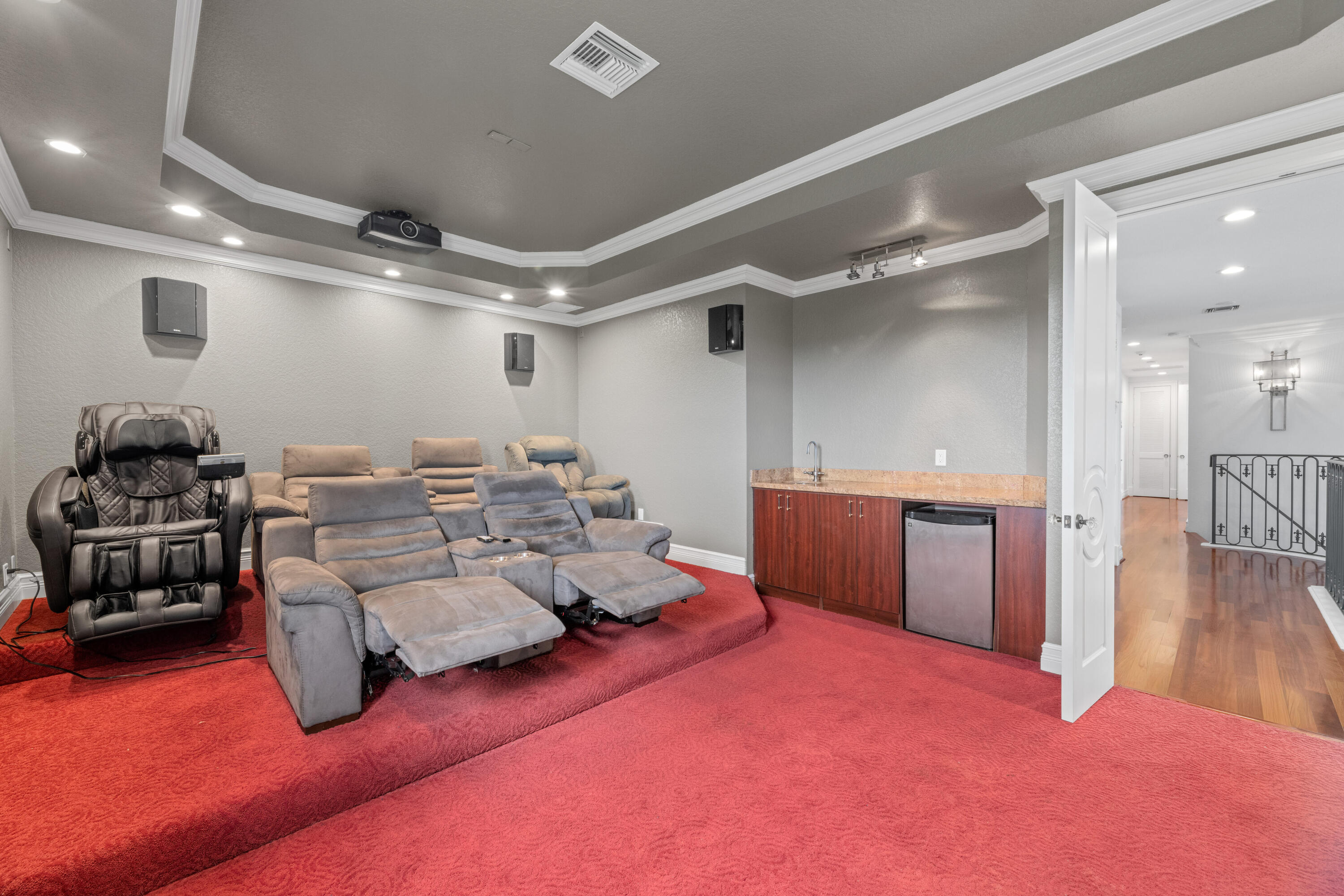 Home theater with gray reclining seats, red carpet, ceiling projector, and a small wet bar.