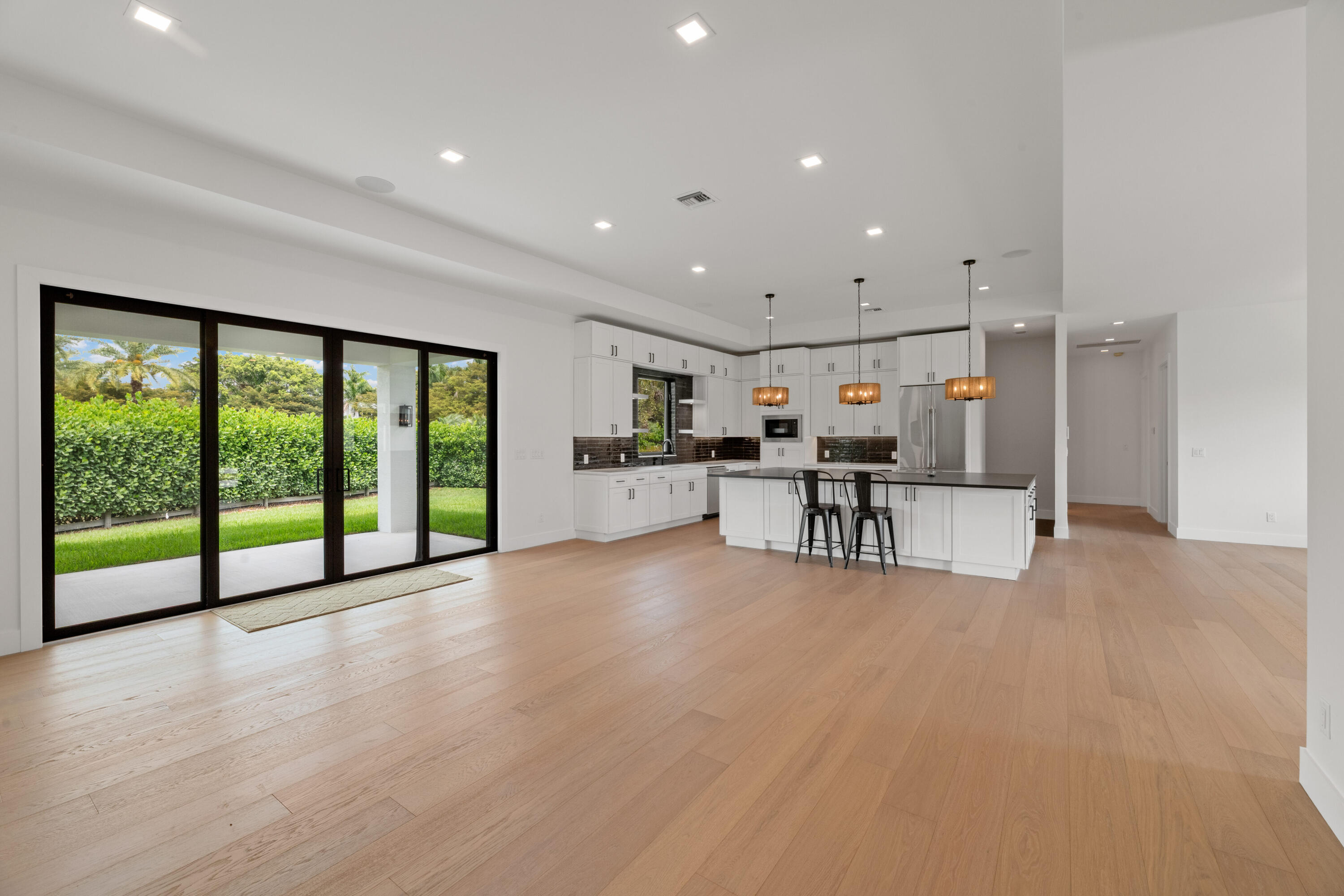 Open kitchen with white cabinetry and island beside sliding glass doors overlooking a hedge and lawn.