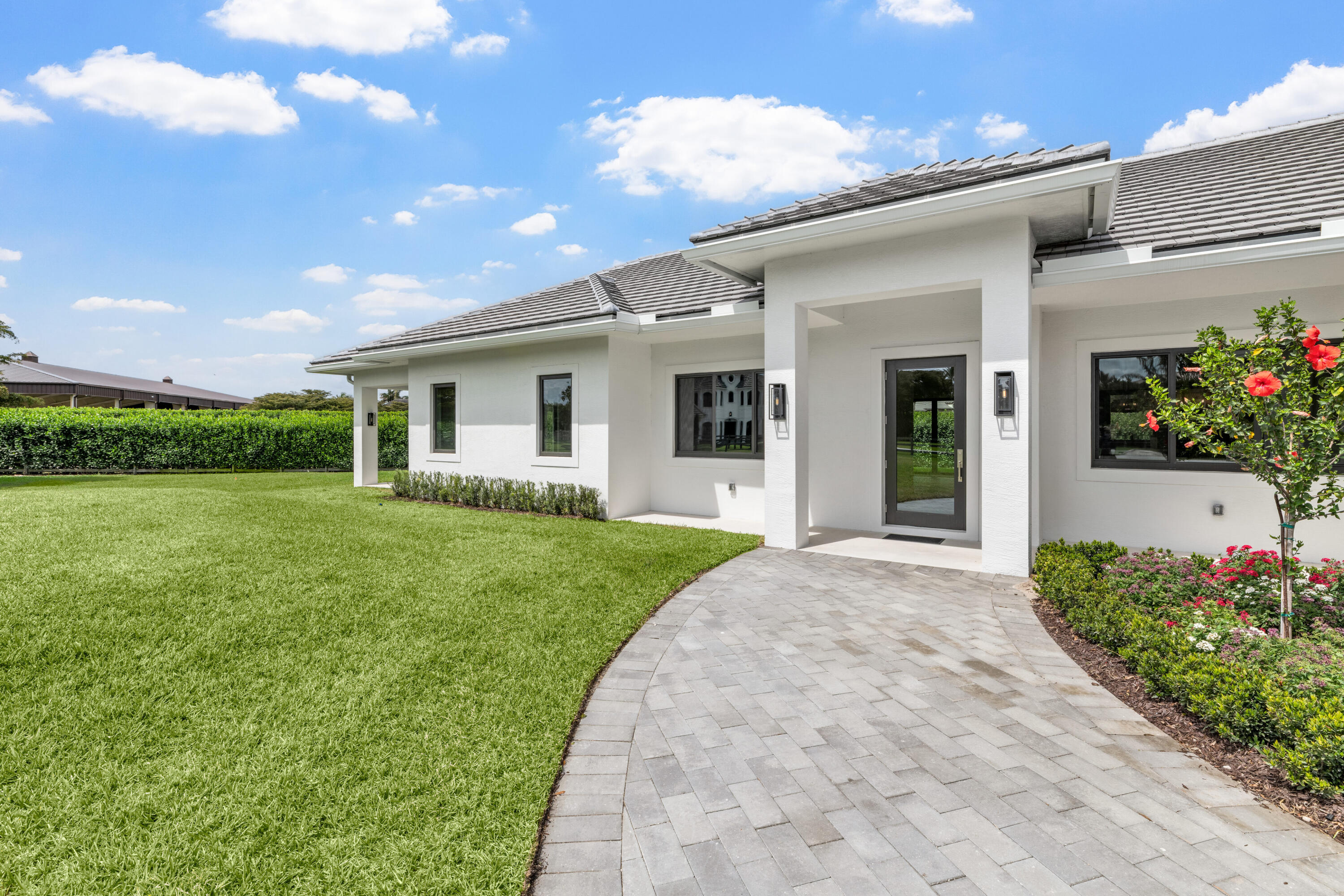 Modern white home with a covered entry, curved paver walkway, broad lawn, and flowering shrubs.
