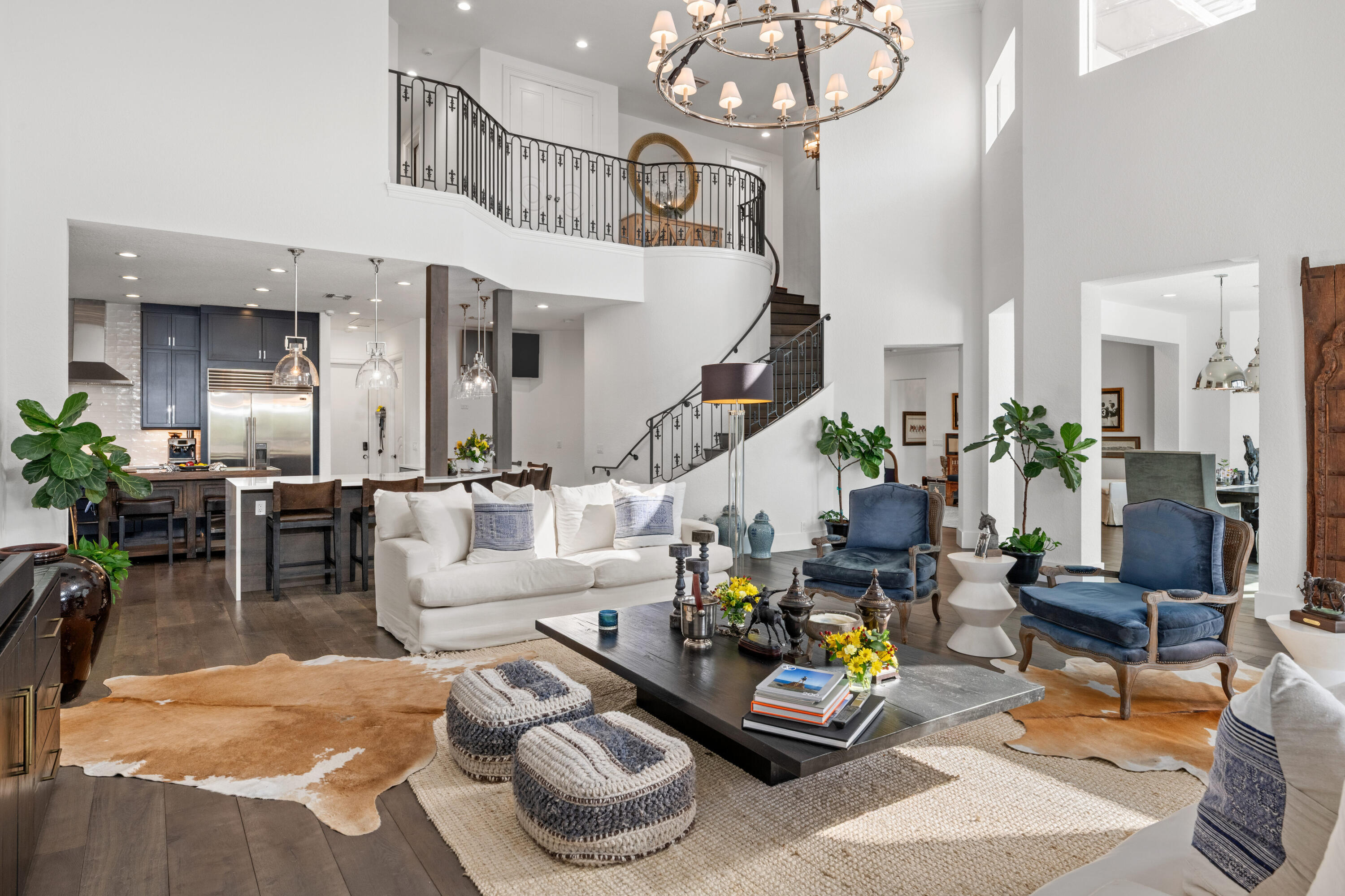 Open-plan living room with a white sofa, blue armchairs, and a curved staircase overlooking the space.