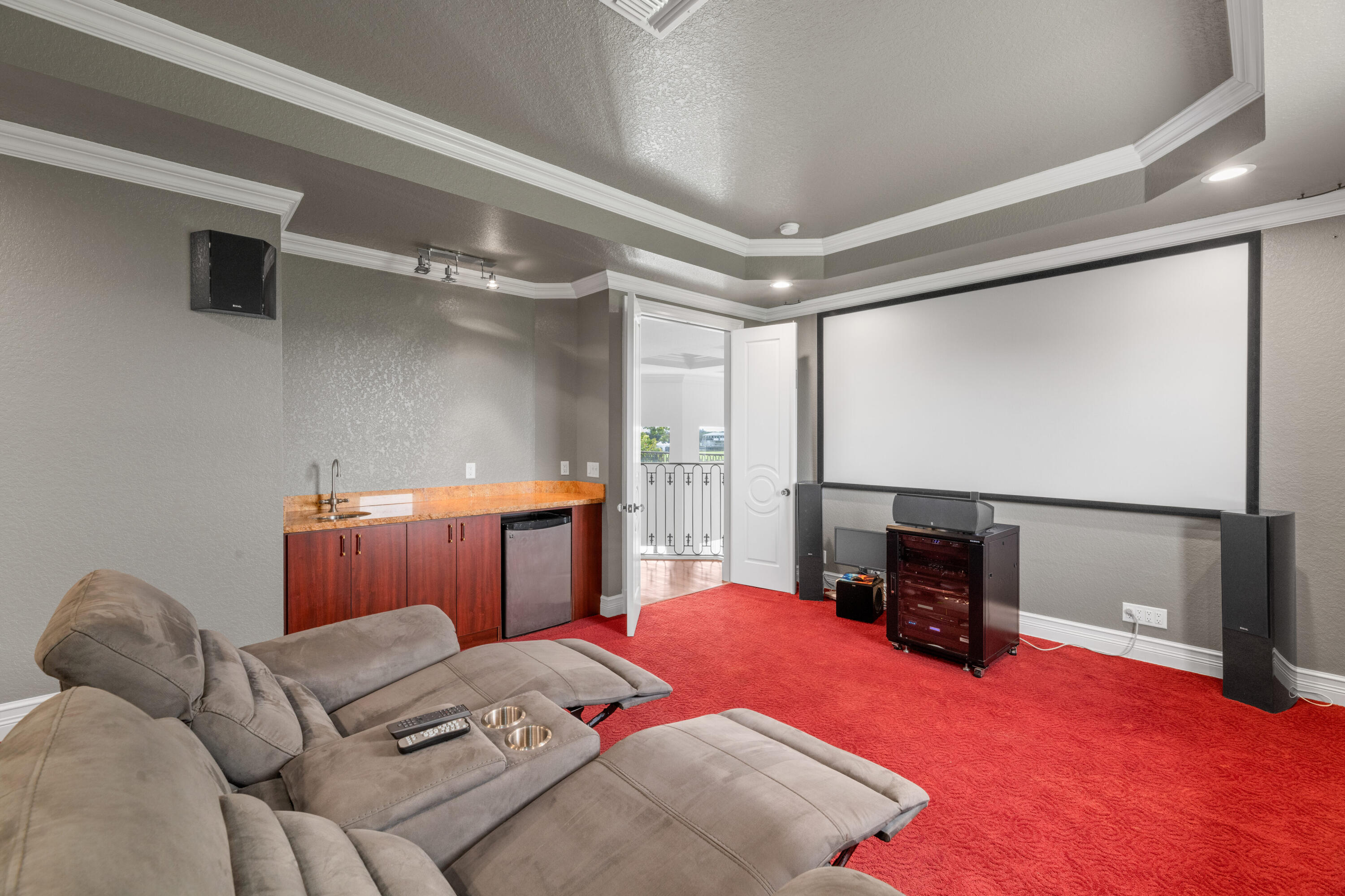 Home theater with a large projection screen, gray reclining sectional, red carpet, and wet bar.