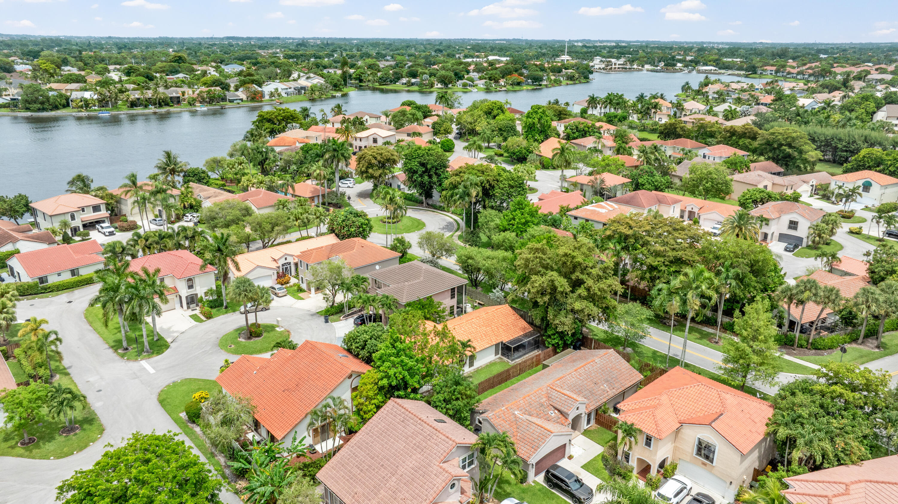 Aerial neighborhood view with terracotta-roofed homes, winding streets, and a lake.