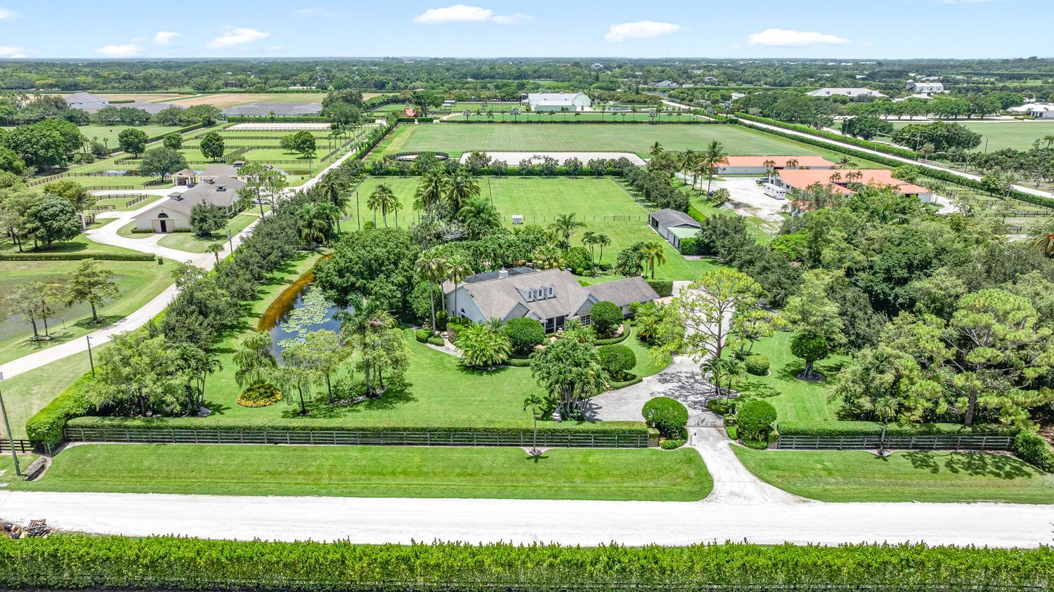 Aerial view of an equestrian estate with a landscaped home, fenced paddocks, riding arenas, and barns.