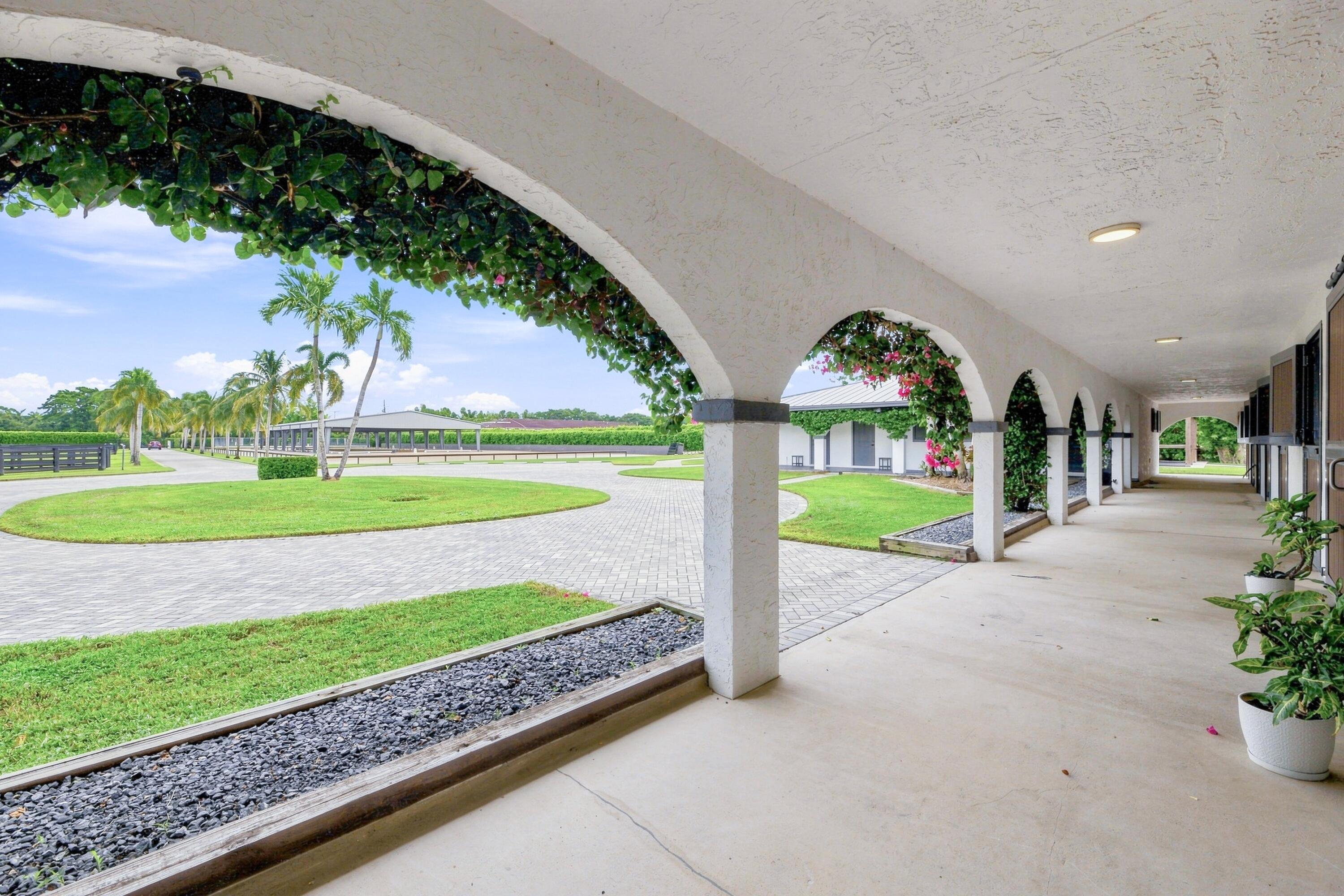 Arched covered porch overlooking a palm-lined lawn and curved paved drive.