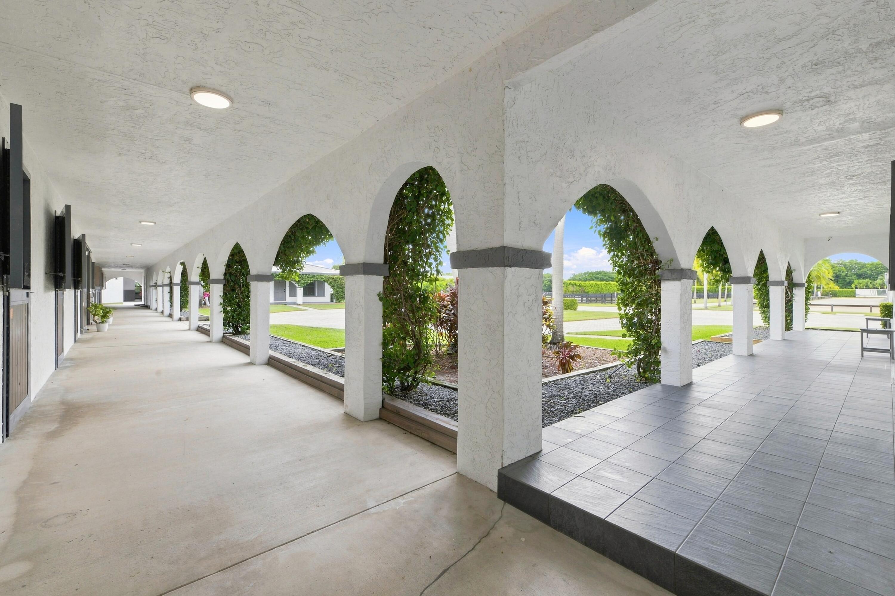 Covered patio with vine-covered white arches and a tiled terrace overlooking landscaped grounds.