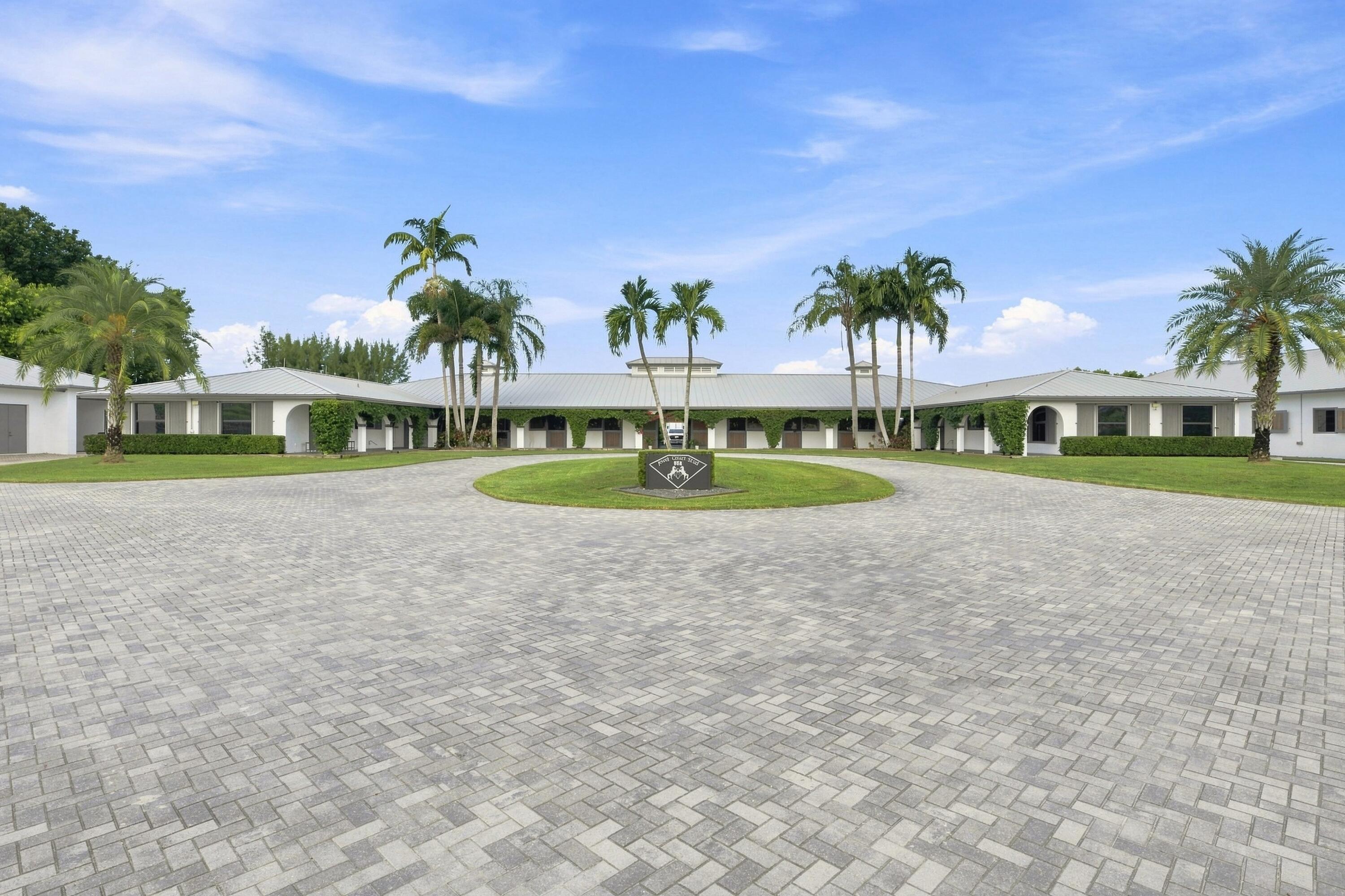 Single-story white building with palm trees behind a circular paved driveway and central lawn.