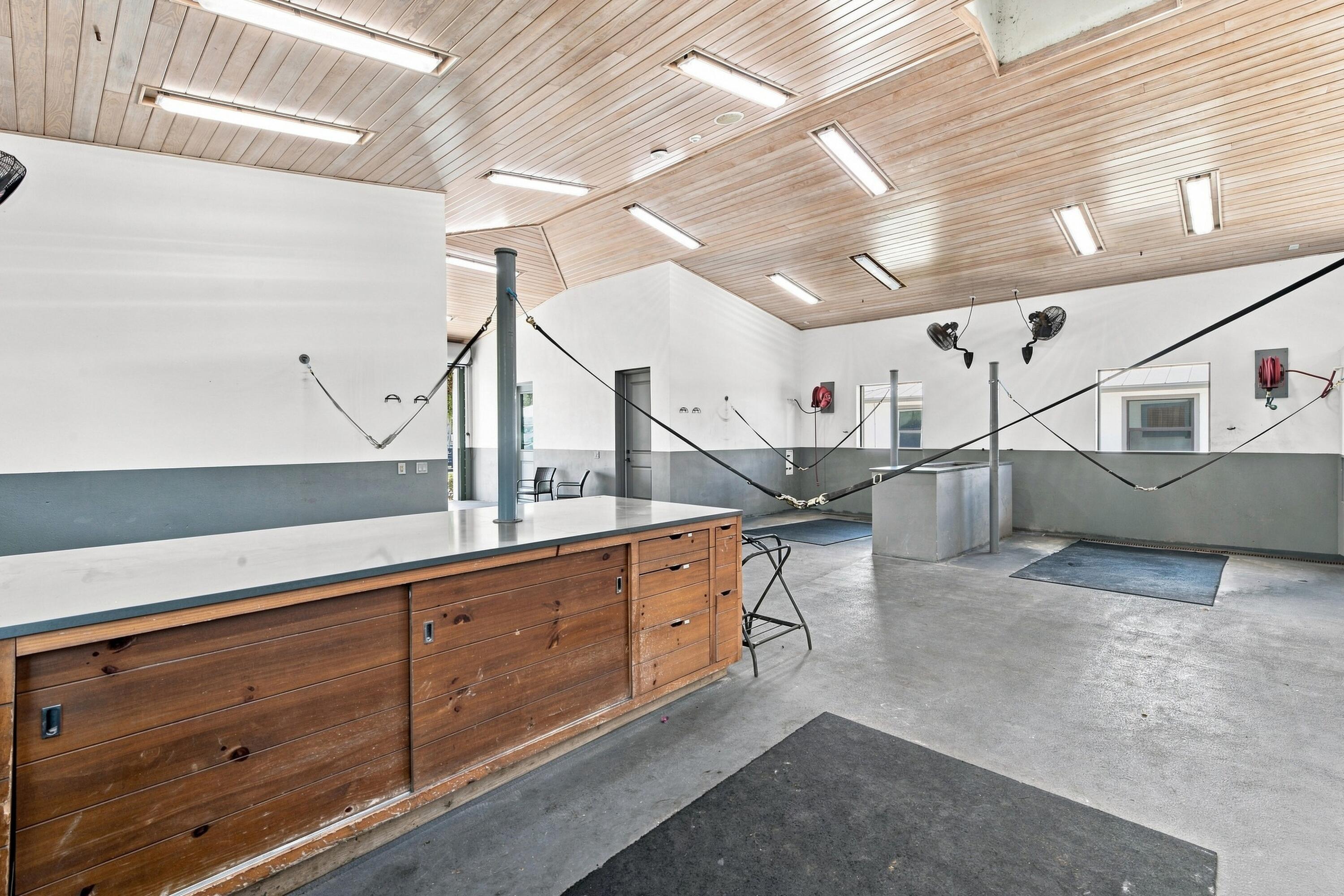 Equestrian grooming area with cross-ties, a wooden counter, concrete floor, and wood-plank ceiling.