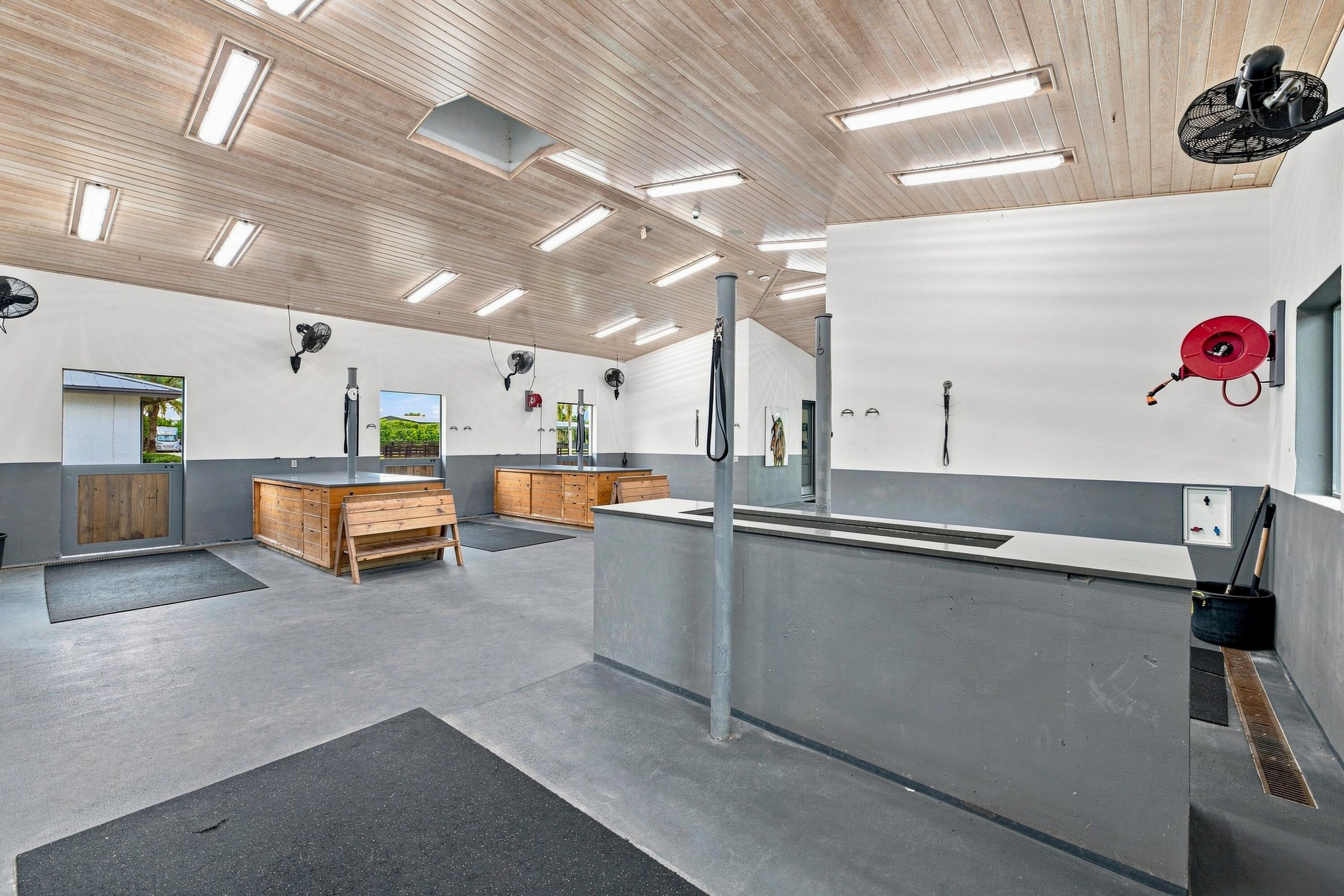 Equestrian wash area with long wash bays, wooden cabinets and benches, and a wood-paneled ceiling.