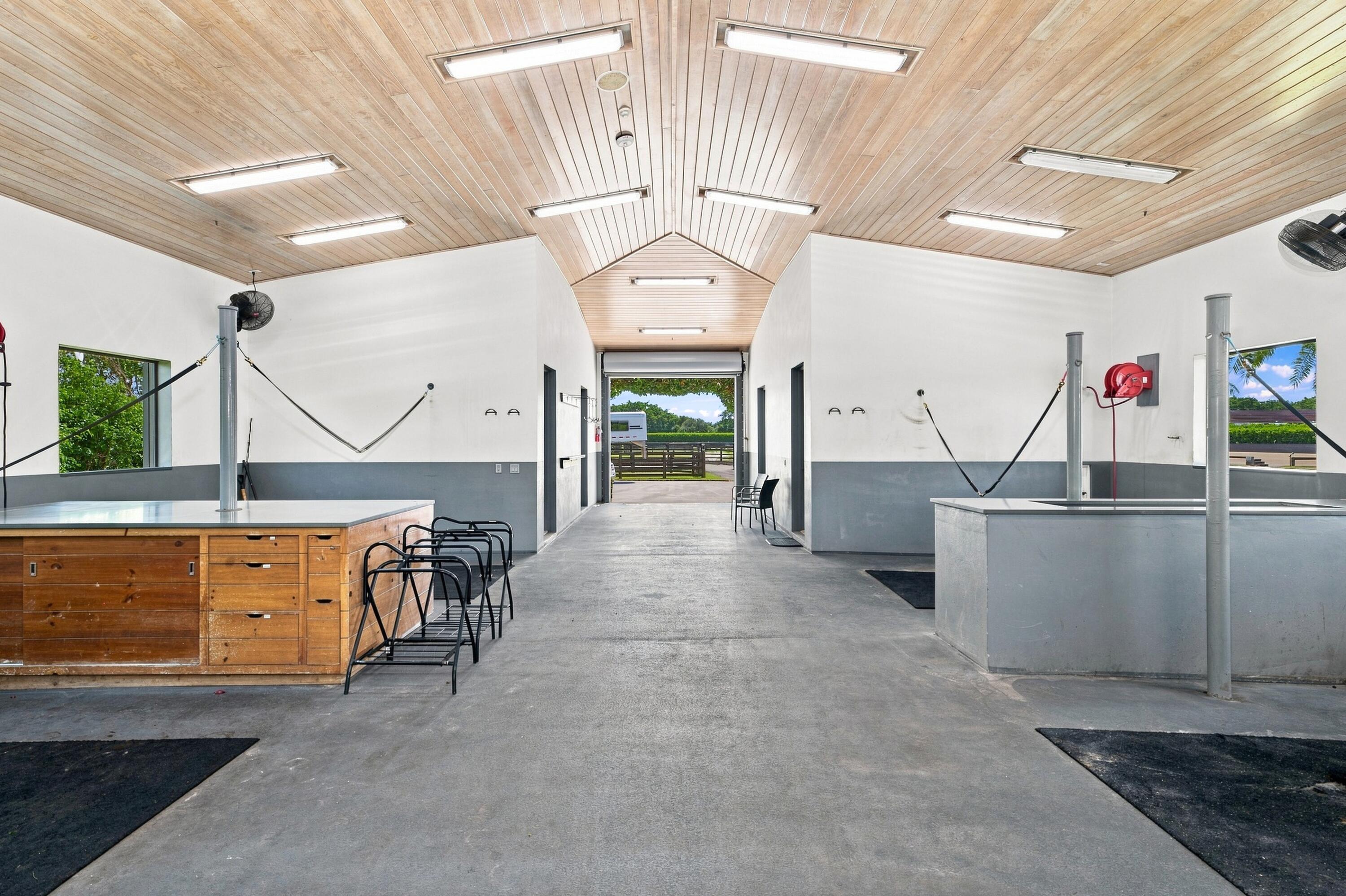 Equestrian wash bay with concrete floors, cross-ties, and a high wood-plank ceiling.