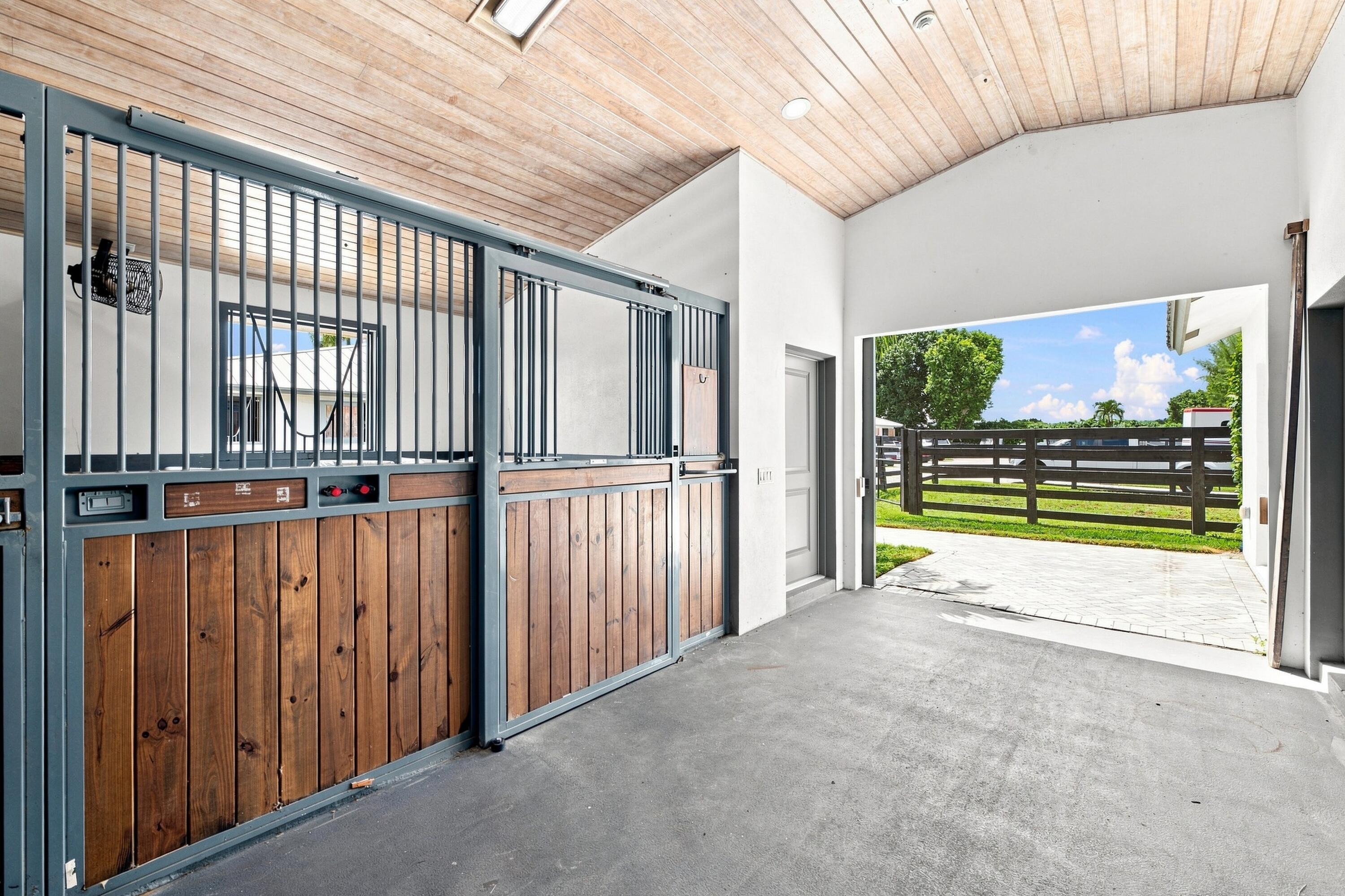 Equestrian stable with wood-and-metal stalls and an open doorway to a fenced paddock.
