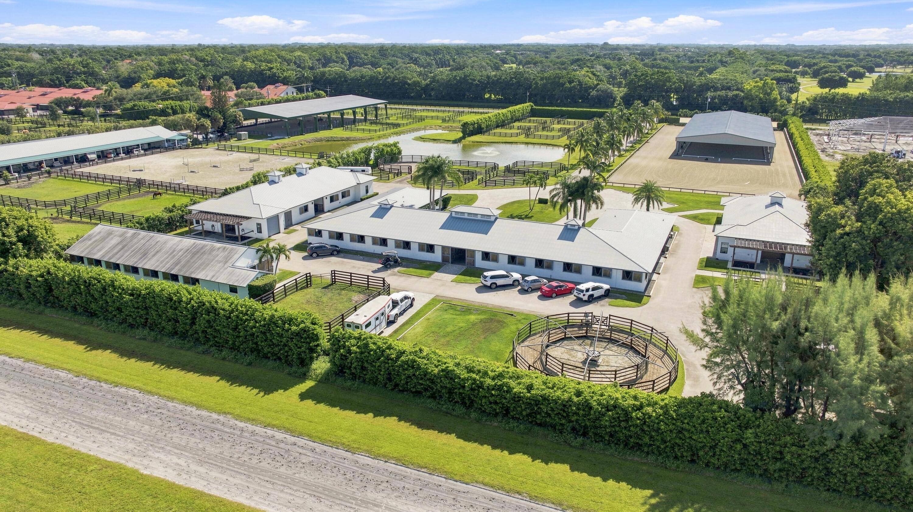 Aerial view of an equestrian property with fenced paddocks, riding arenas, a pond, and a round pen.