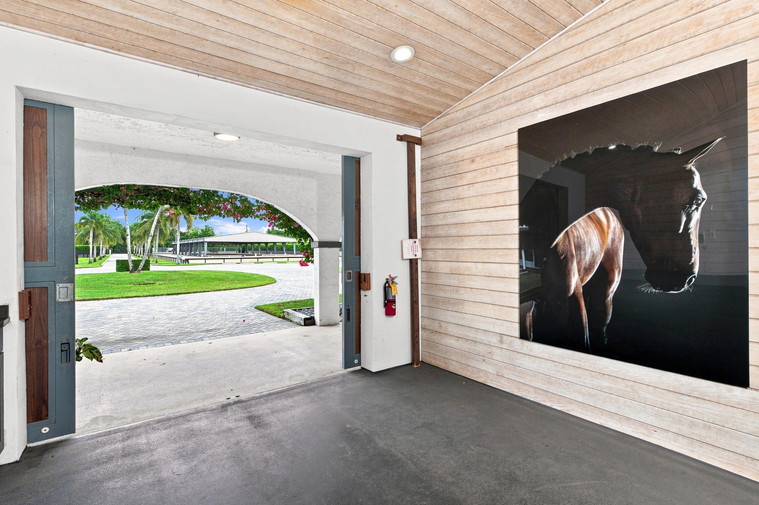 Wood-paneled equestrian bay opens onto a landscaped courtyard, with a large horse photograph on the wall.