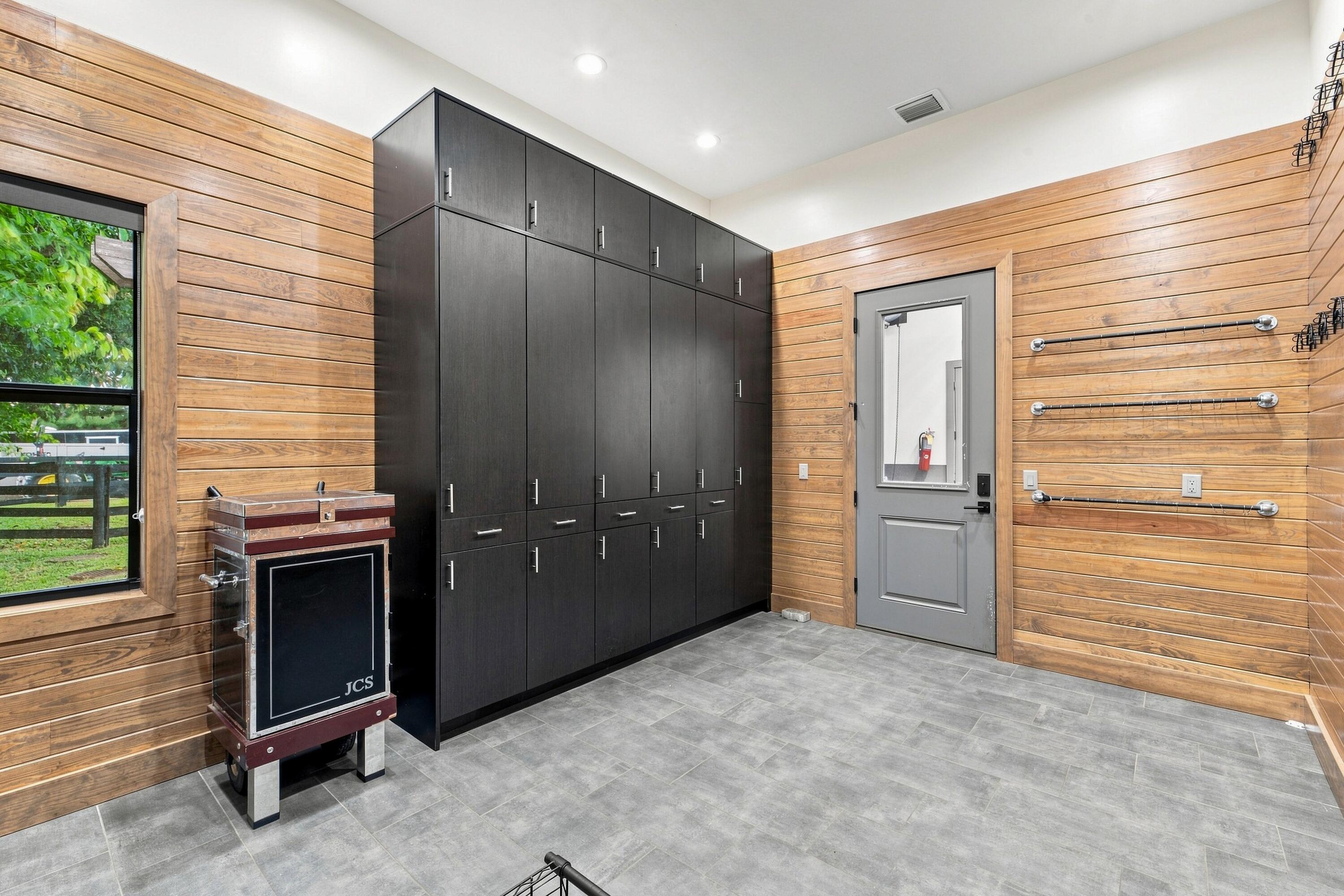Tack room with dark built-in cabinets, wood-plank walls, tiled floor, and wall-mounted hanging rails.