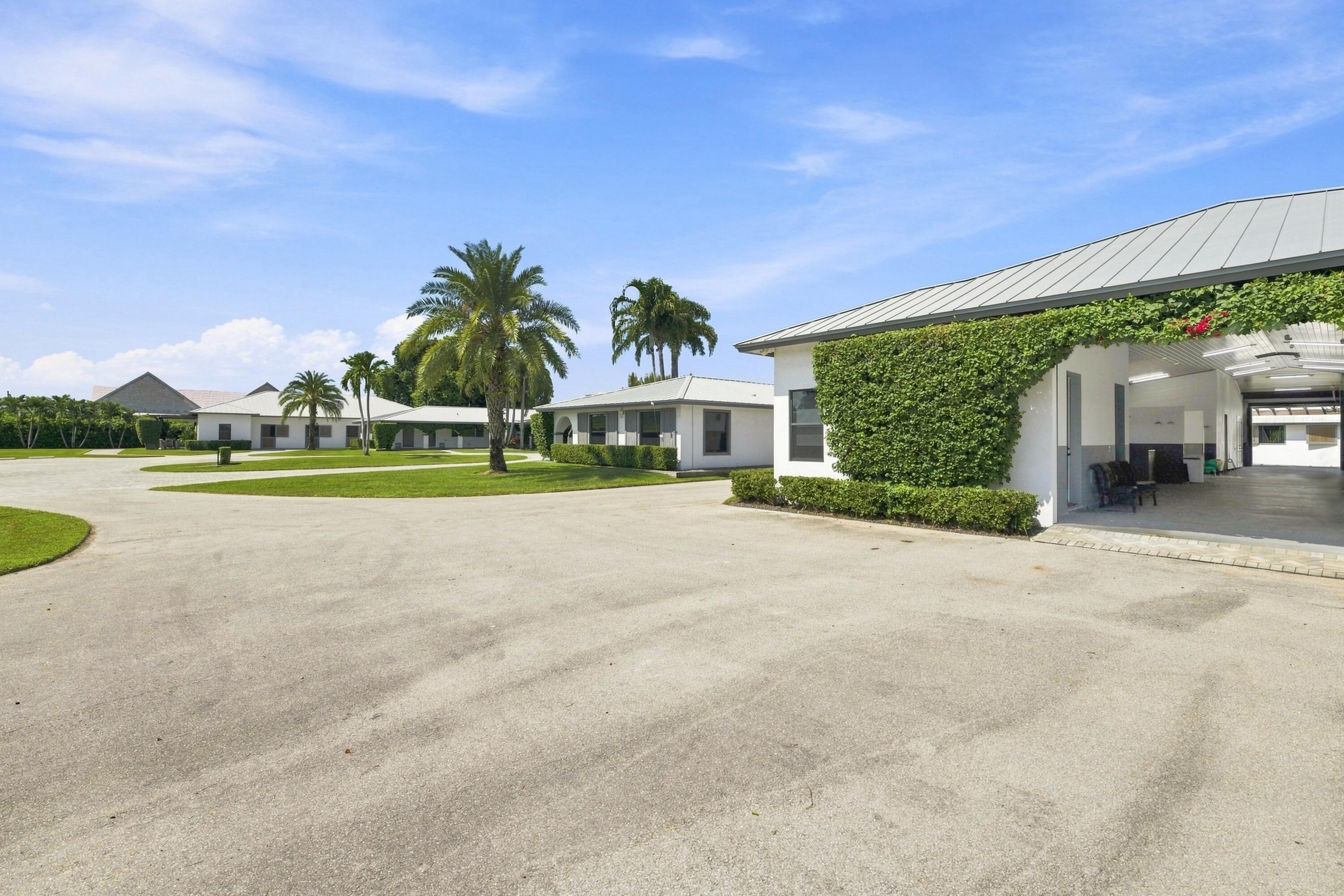 White buildings and palm trees surround a broad paved drive beside a vine-covered open-sided structure.
