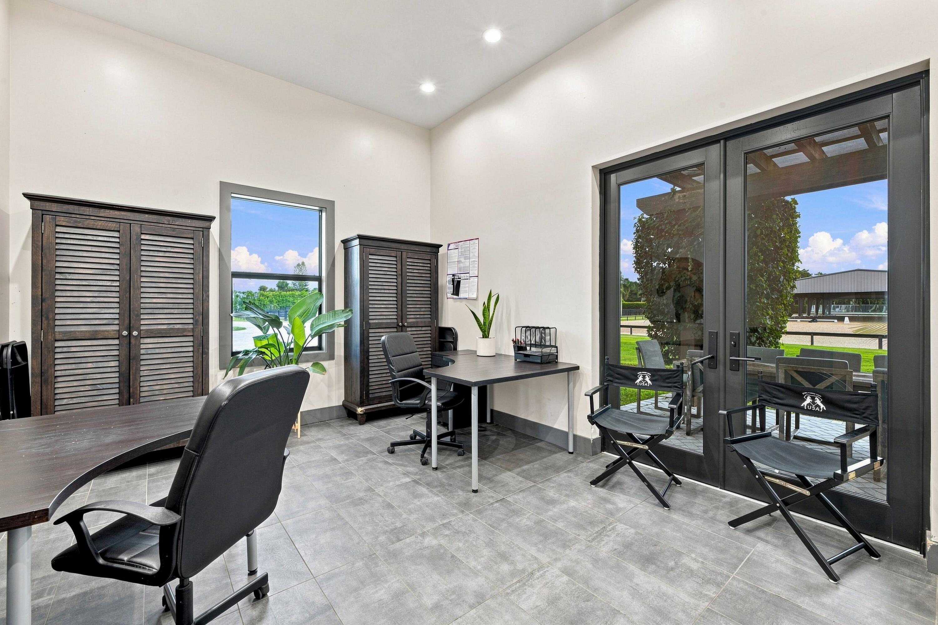 Furnished office with dark louvered cabinets and glass doors overlooking a lawn and covered arena.