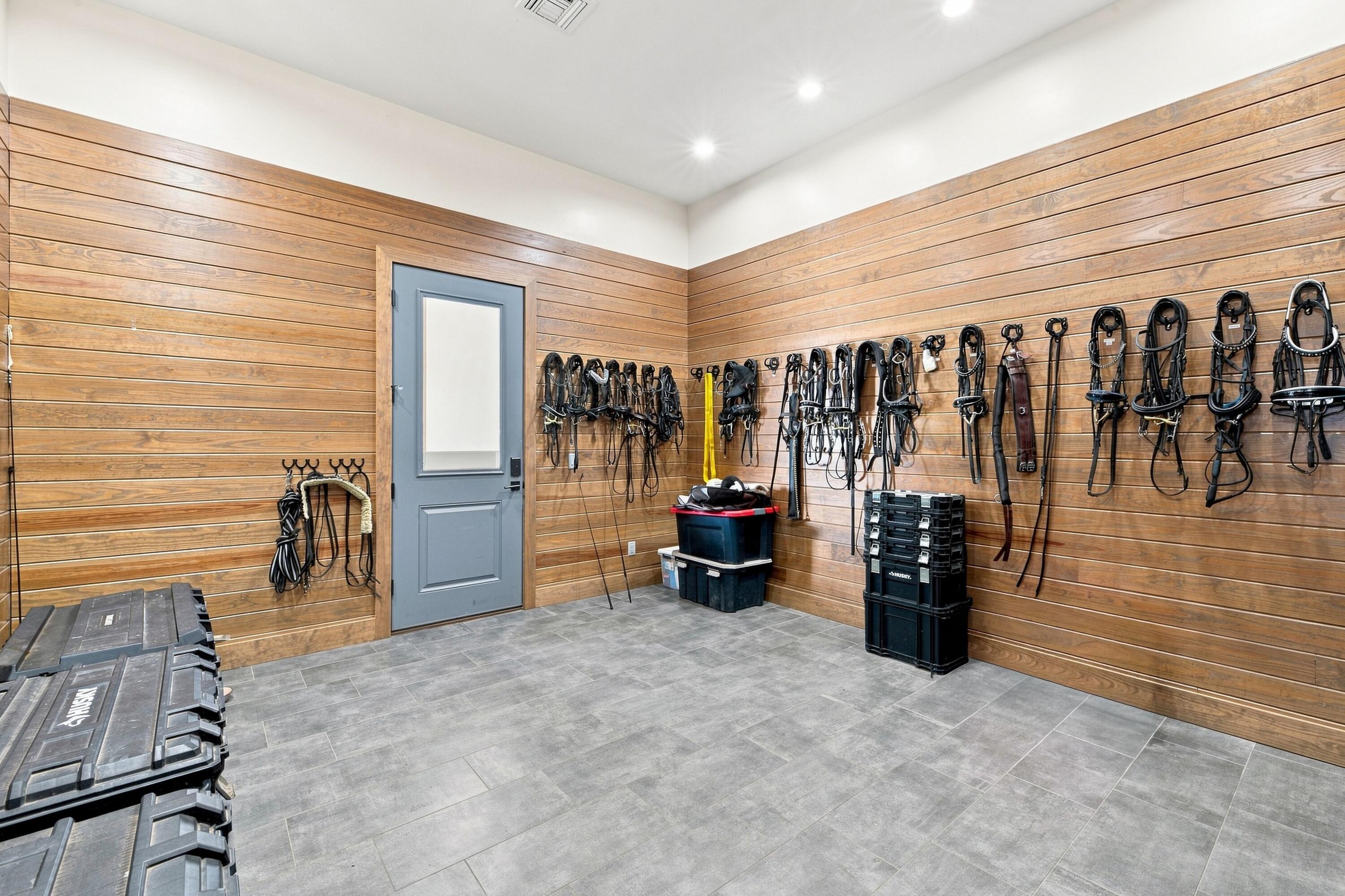 Tack room with rows of horse bridles and reins hanging on wood-plank walls.