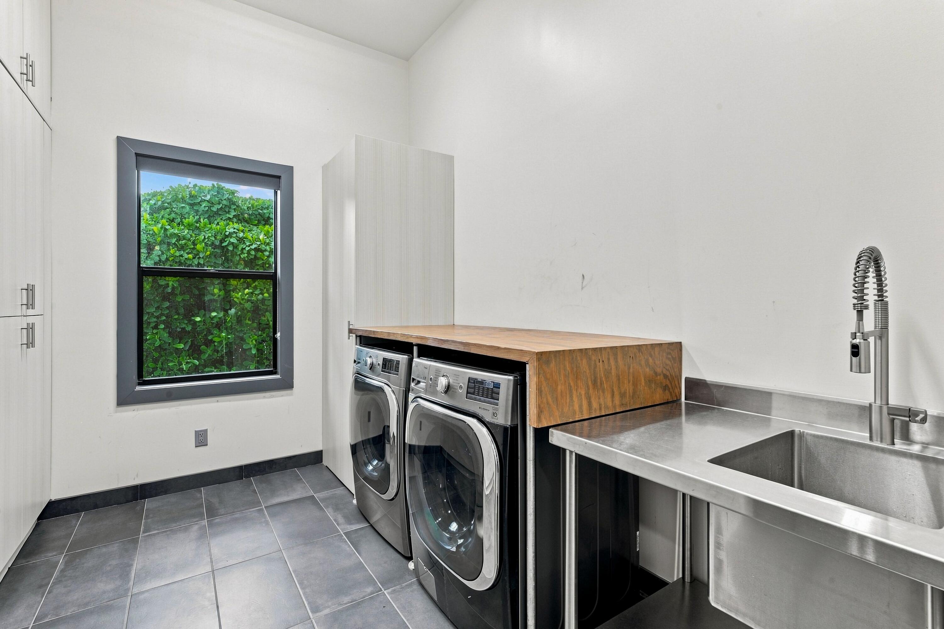 Laundry room with front-loading washer and dryer, wood countertop, and stainless-steel utility sink.