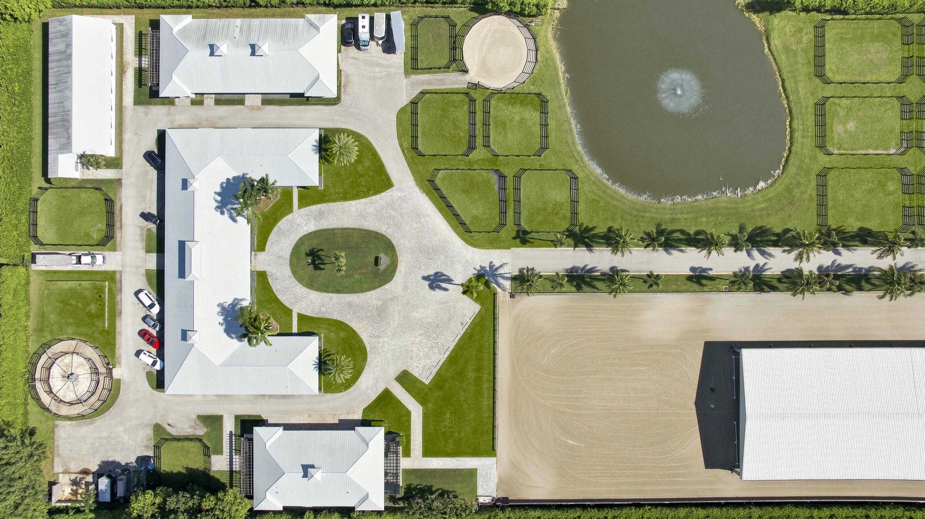 Aerial view of an equestrian property with fenced paddocks, a pond, and a large riding arena.