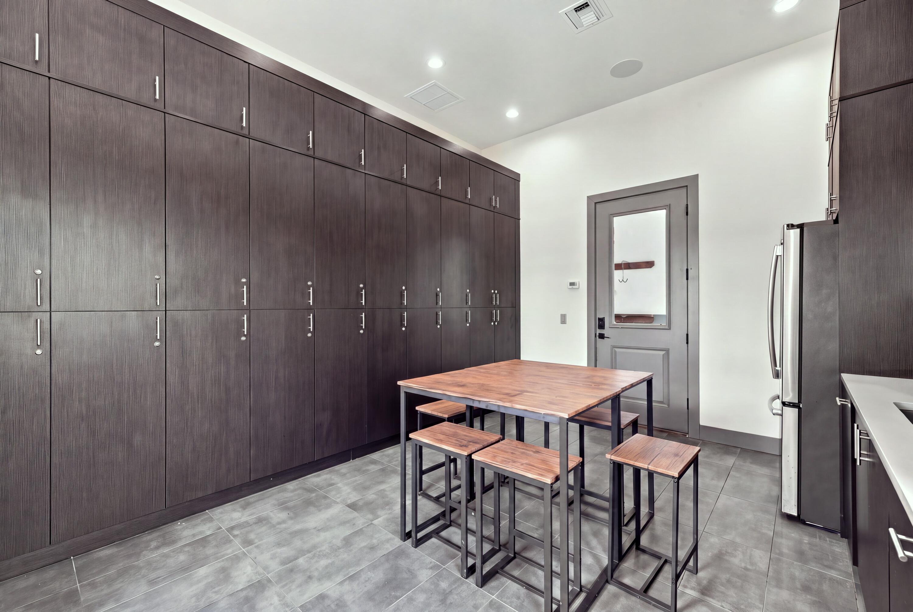 Kitchen with dark floor-to-ceiling cabinets, a stainless steel refrigerator, and a wood-topped table with stools.