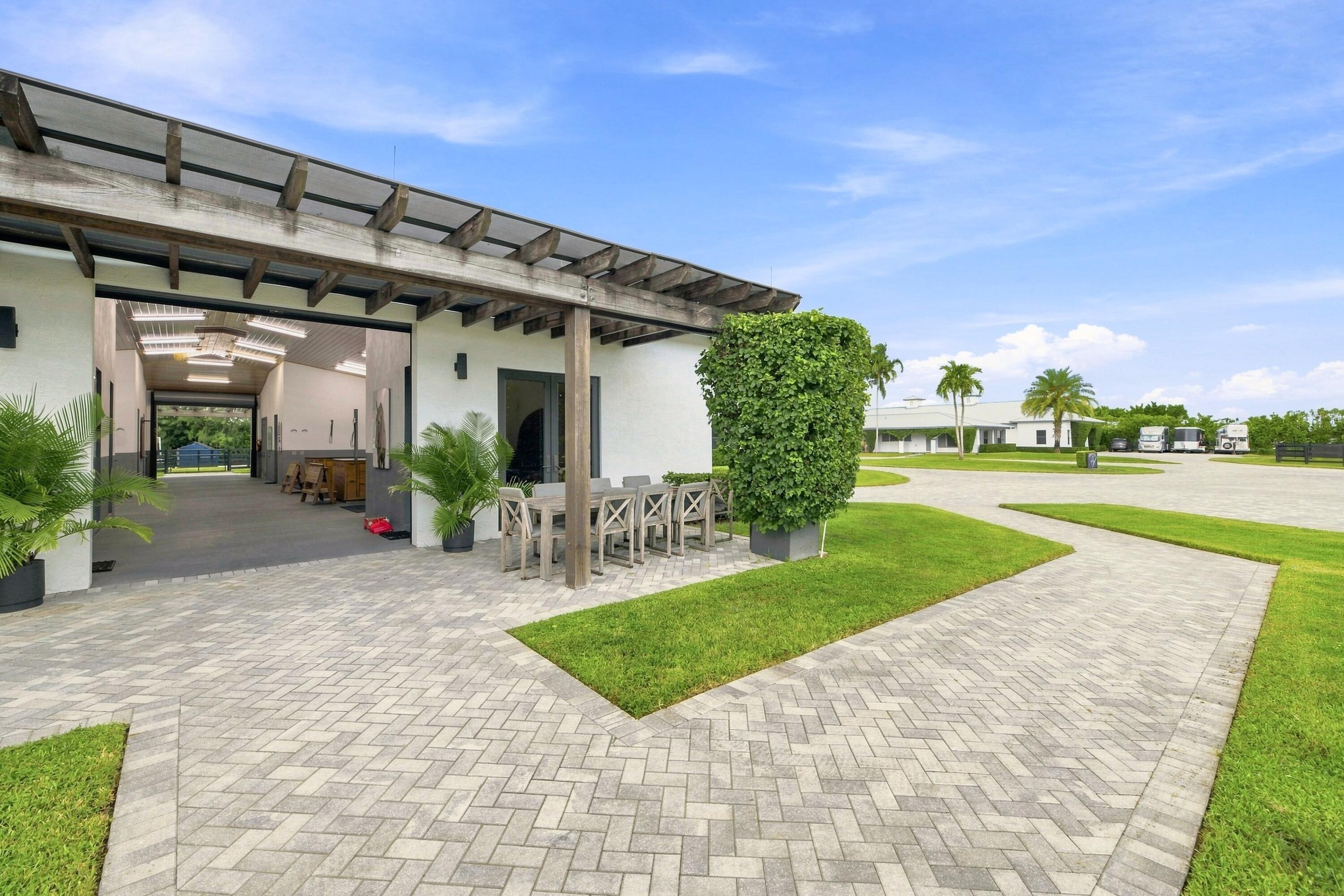 Modern white building with a timber pergola, outdoor dining area, and broad paver courtyard.