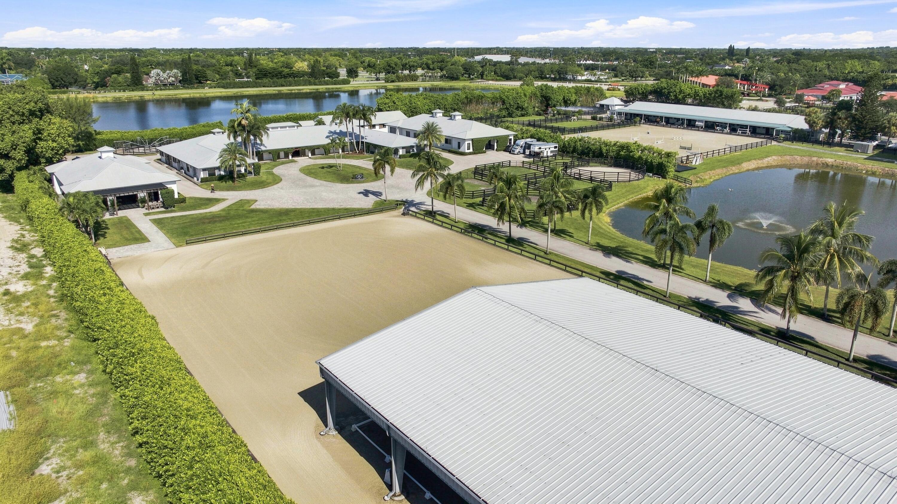 Aerial view of an equestrian estate with fenced arenas, palm trees, and ponds.