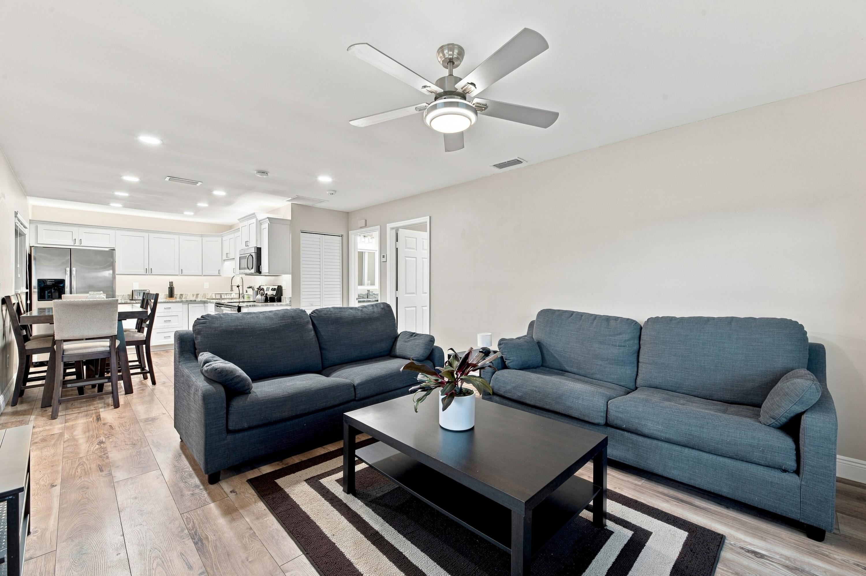 Living room with two blue-gray sofas, a dark coffee table, and an open kitchen and dining area.