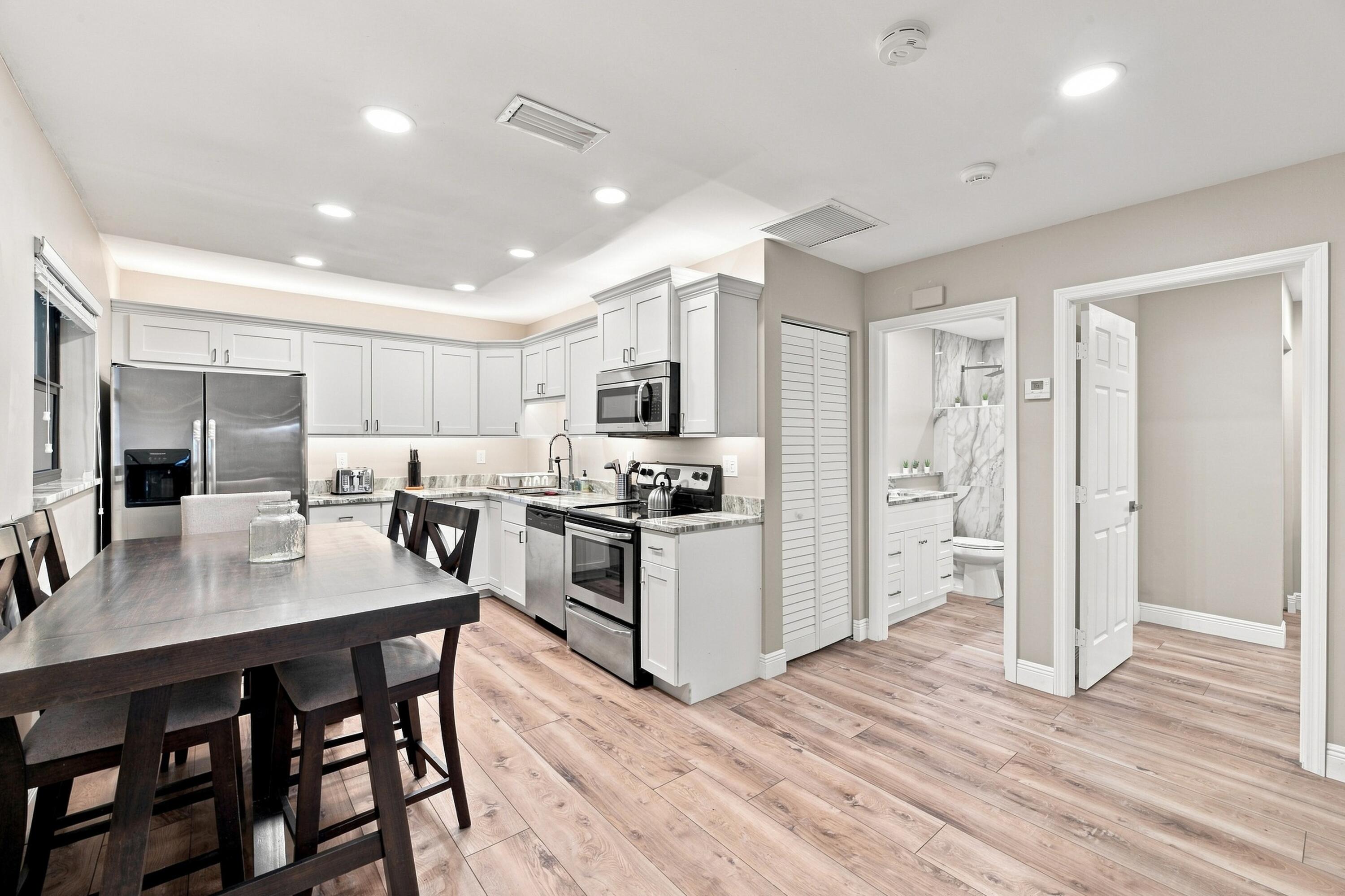Kitchen and dining area with white cabinets, stainless appliances, and a dark table.