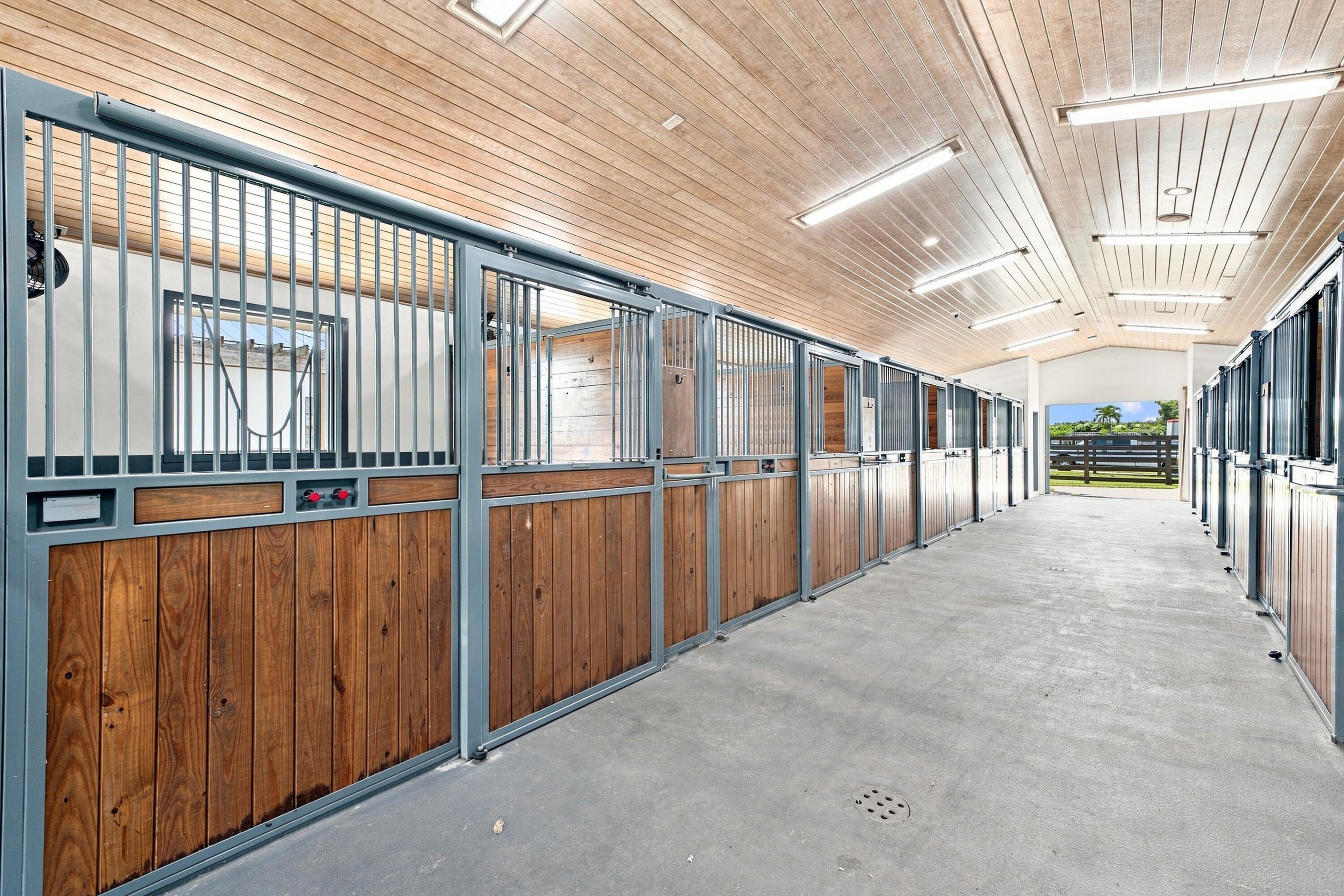 Stable aisle with empty wood-paneled horse stalls and an open view to a fenced paddock.