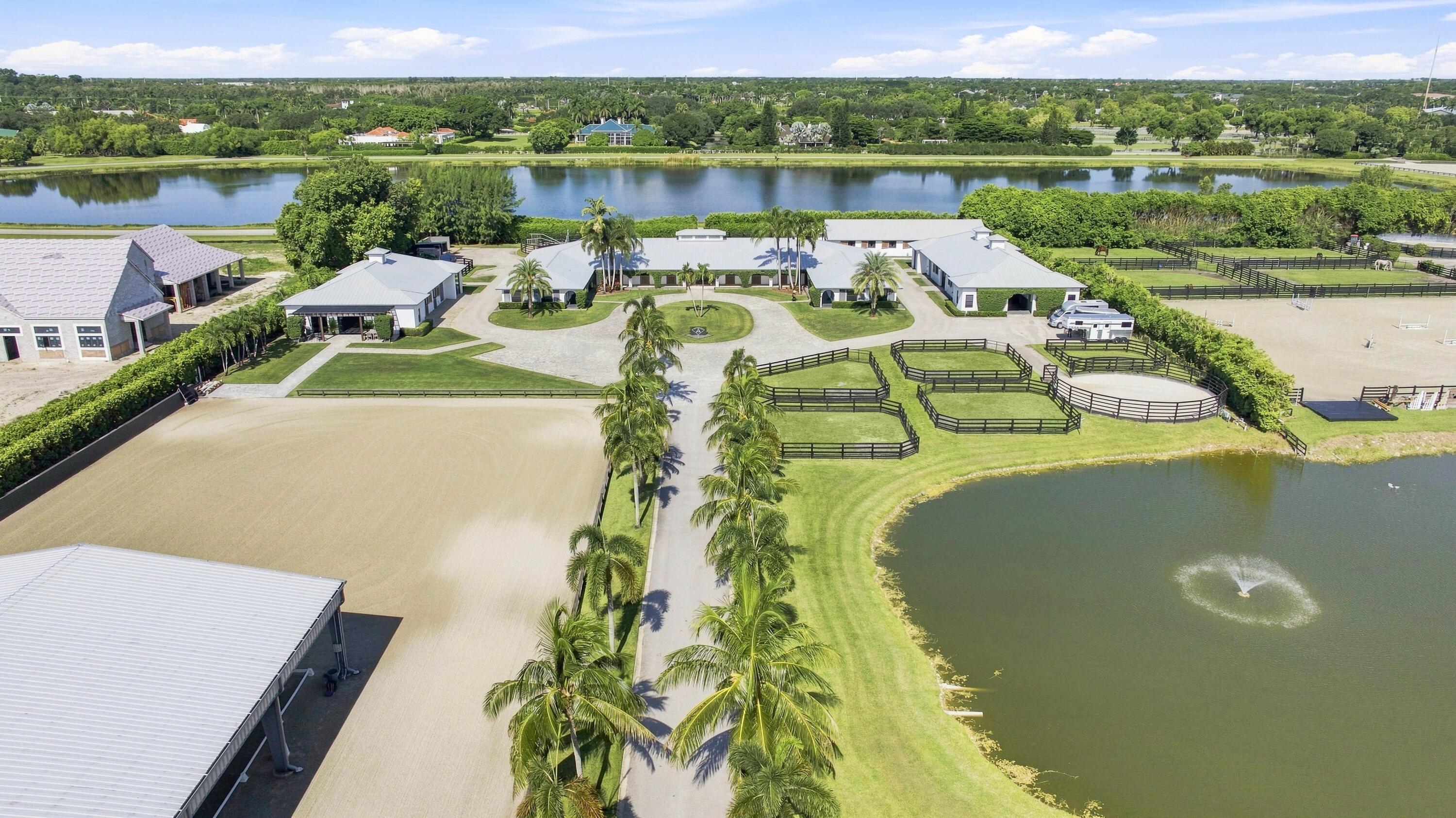 Aerial view of an equestrian estate with fenced paddocks, a riding arena, and a pond with a fountain.