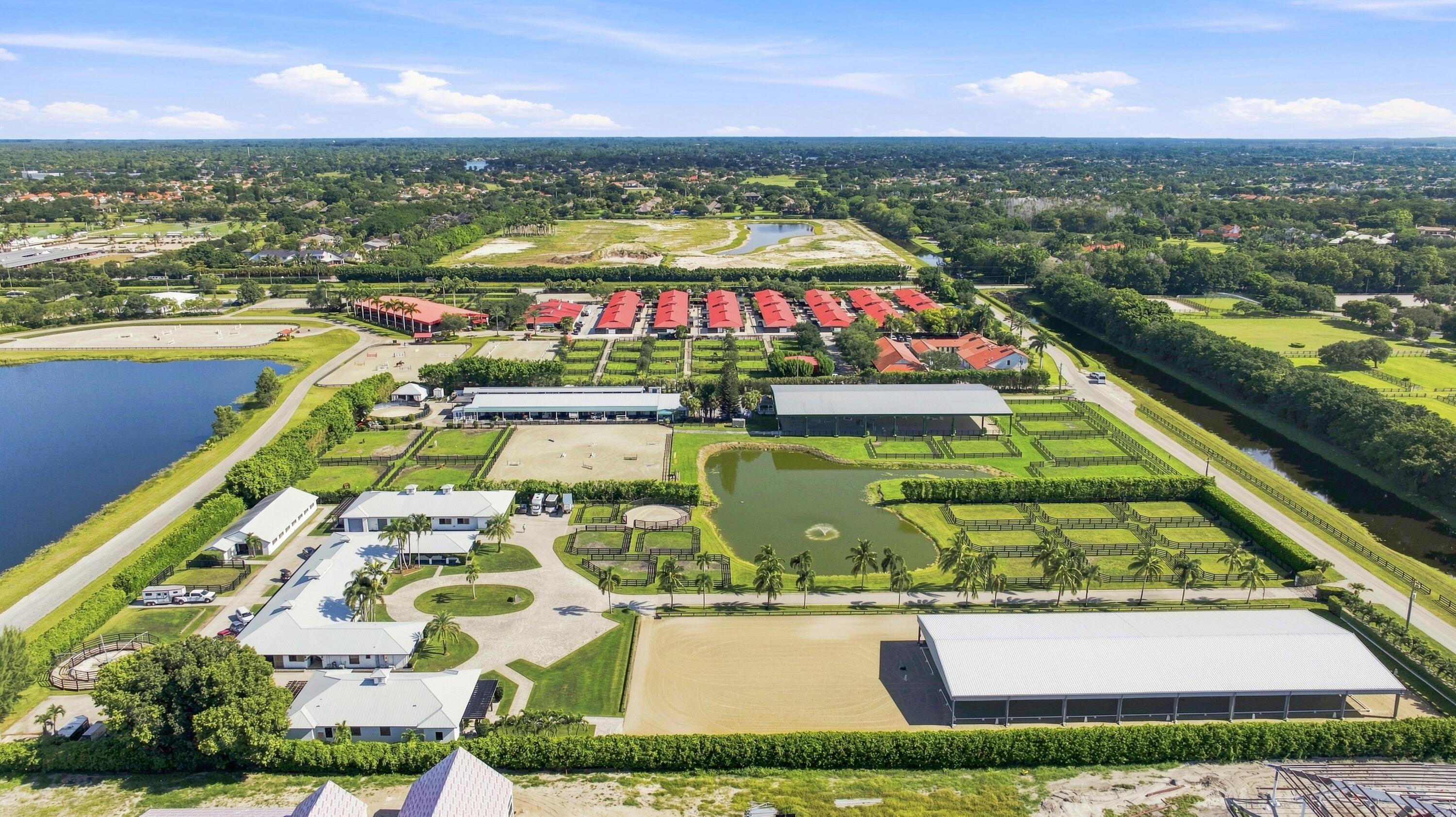 Aerial view of an equestrian property with fenced paddocks, stables, covered arenas, and ponds.