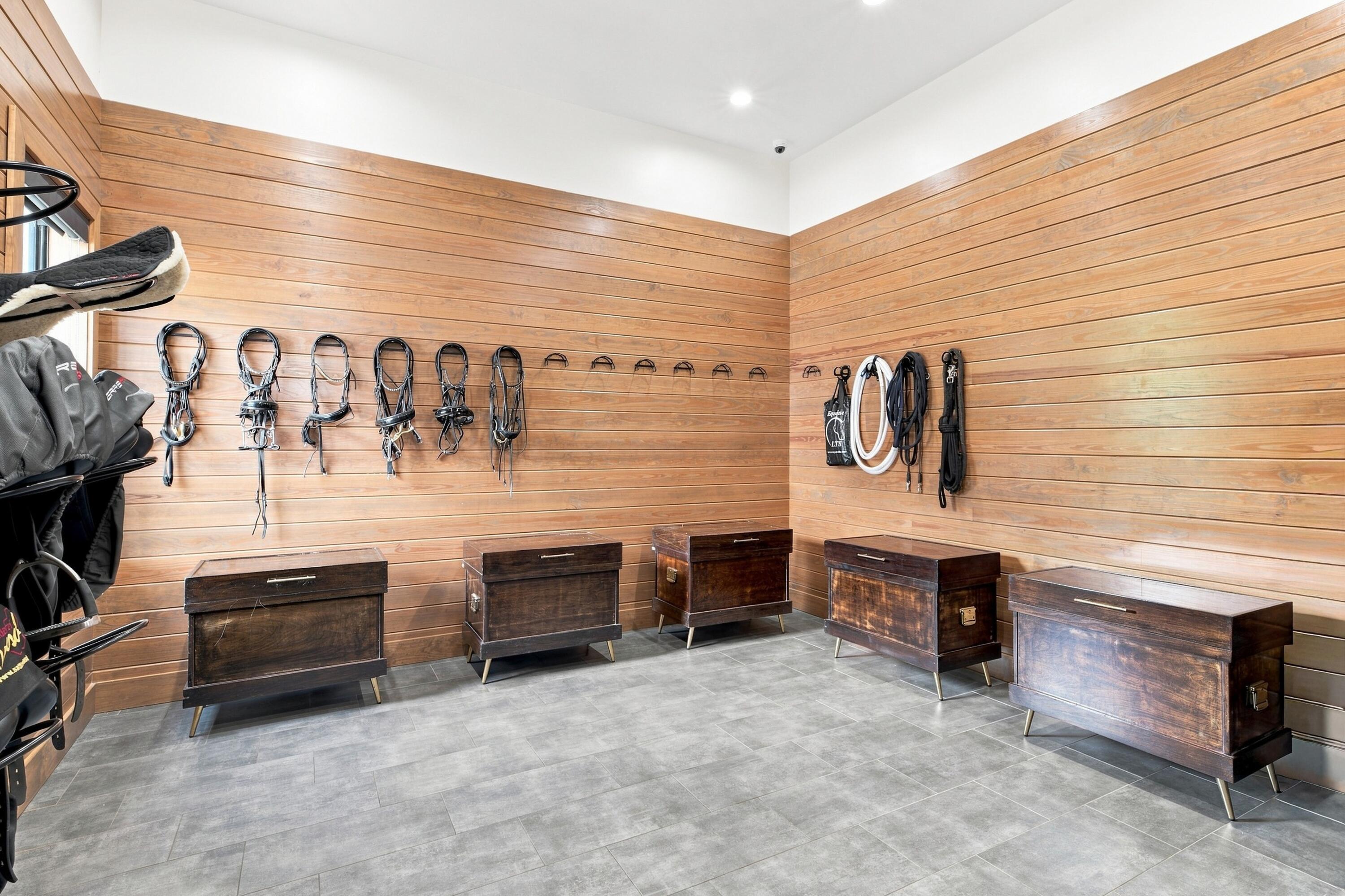 Tack room with bridles on wood-paneled walls and dark wooden storage trunks.