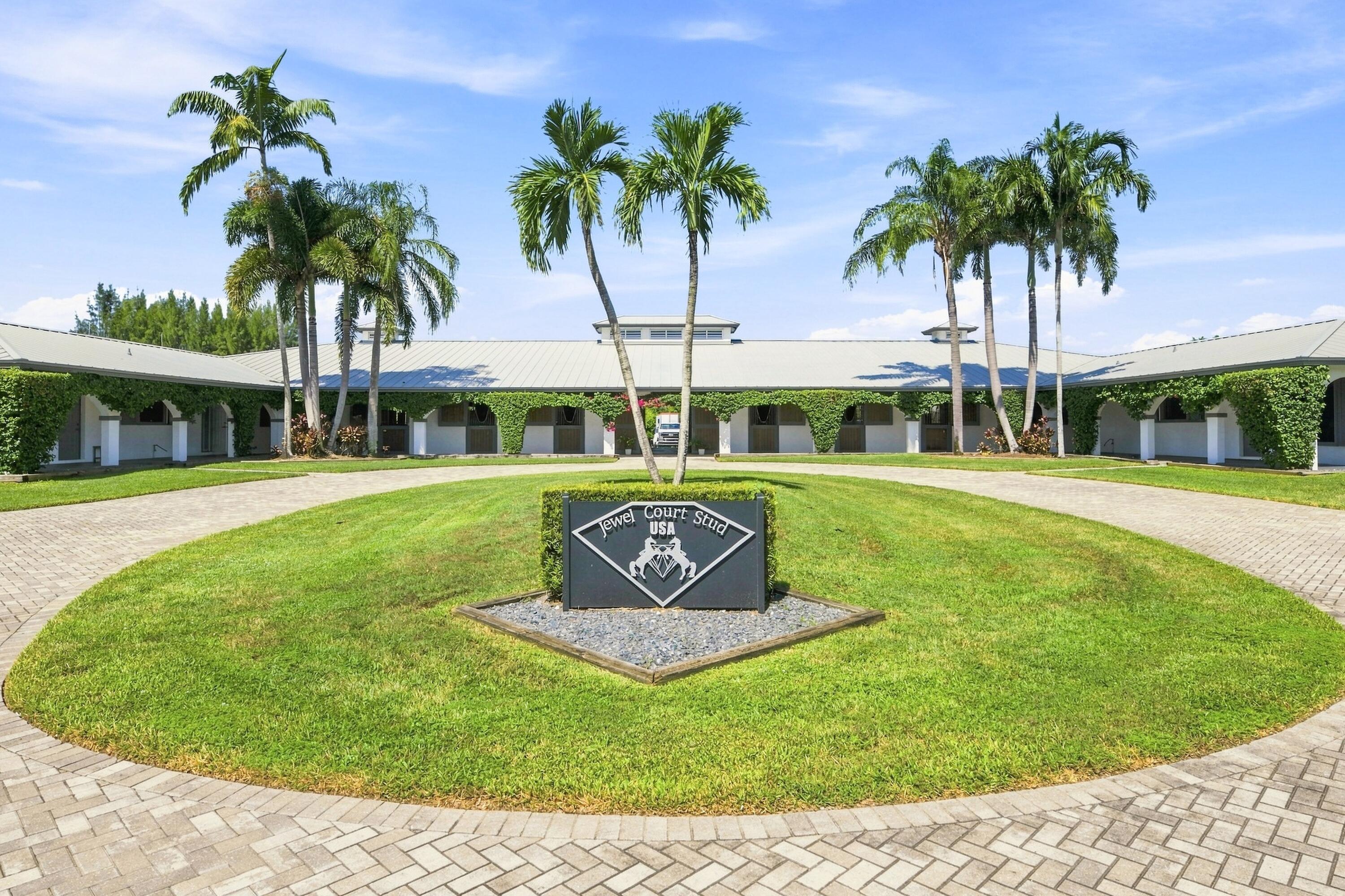 Equestrian stable with a circular paved driveway, palm trees, and a Jewel Court Stud USA sign.