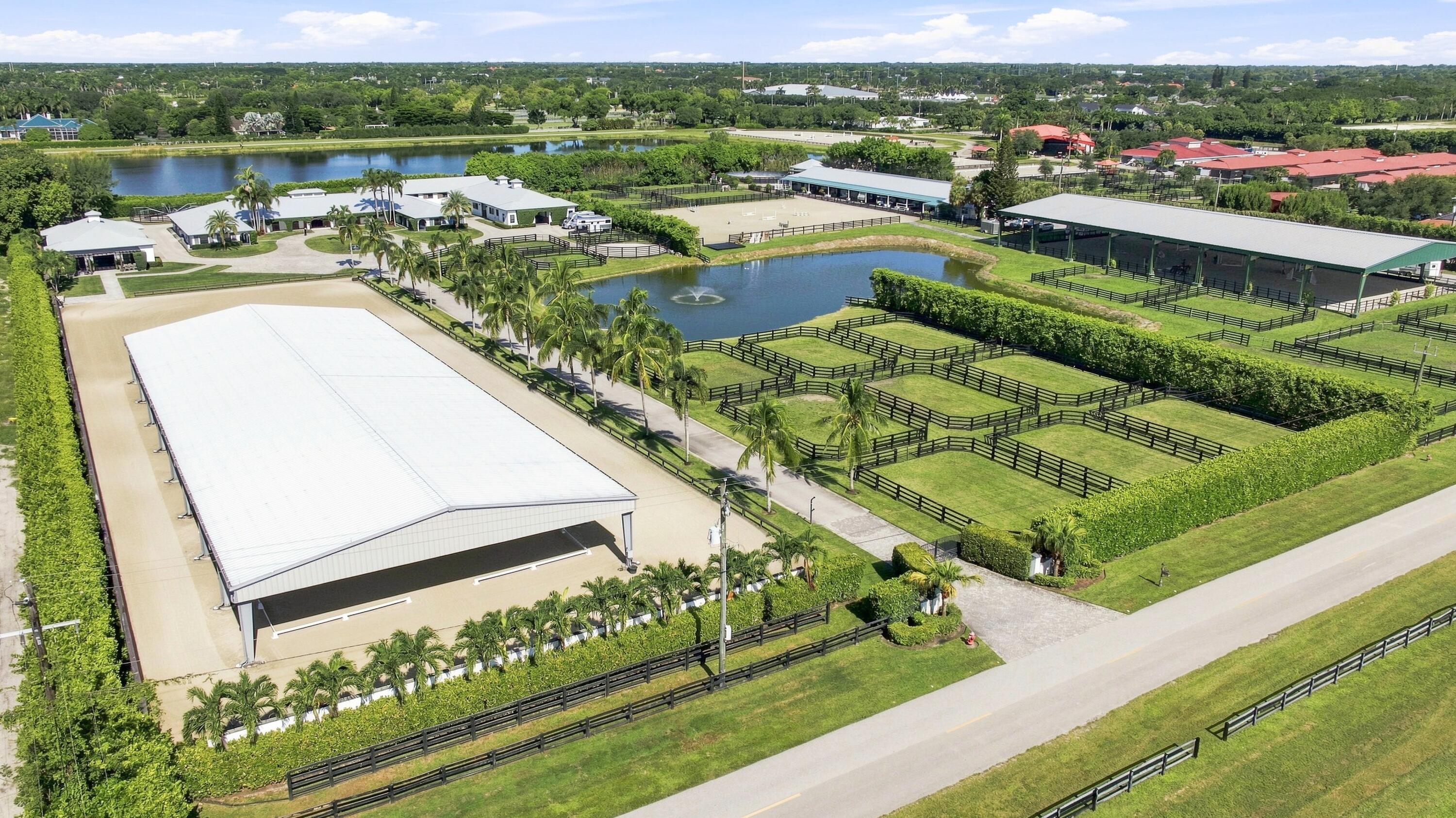 Aerial view of an equestrian property with covered arenas, stables, fenced paddocks, and ponds.