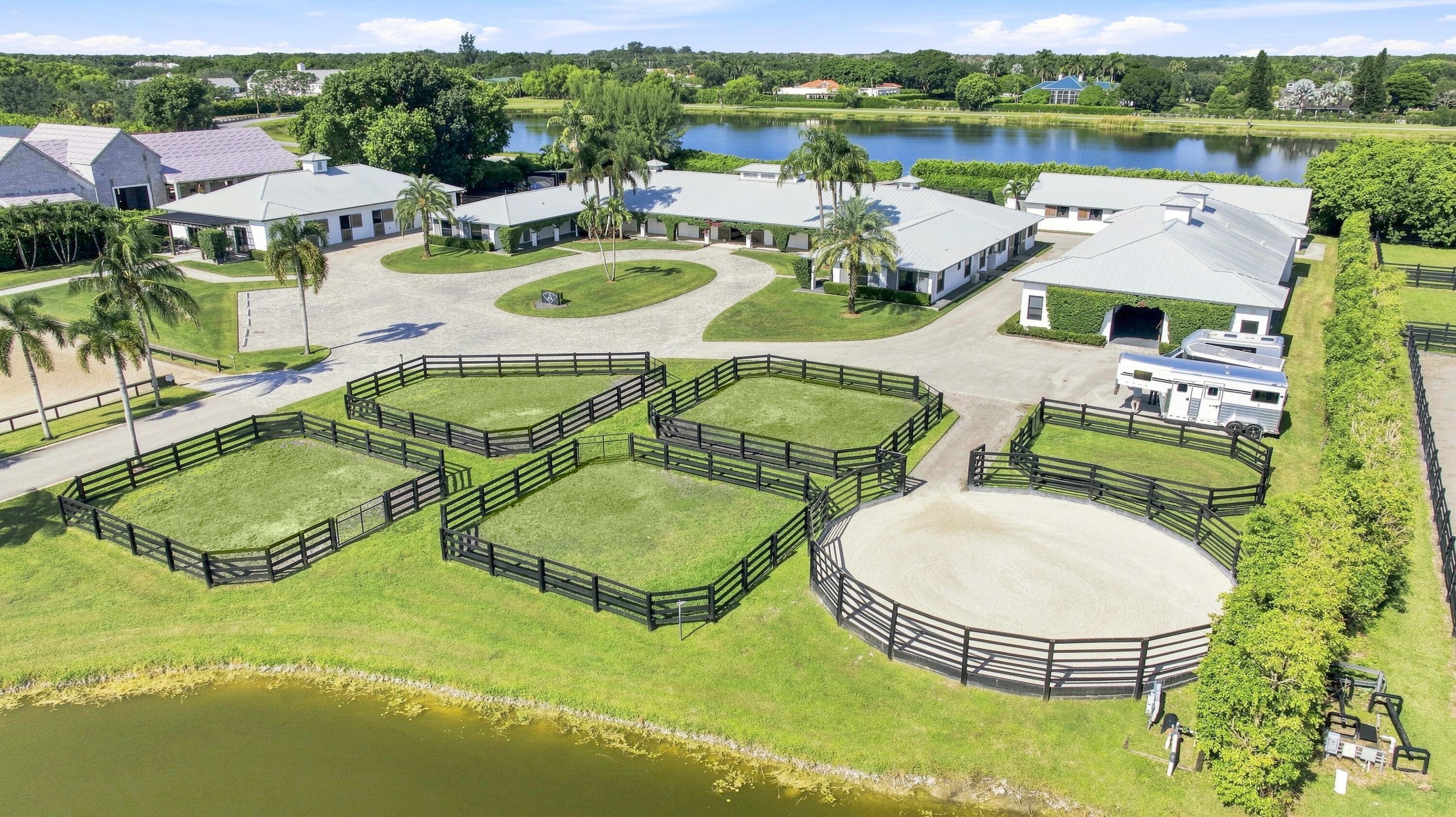 Aerial view of equestrian property with barns, fenced paddocks, a riding arena, and a lake.