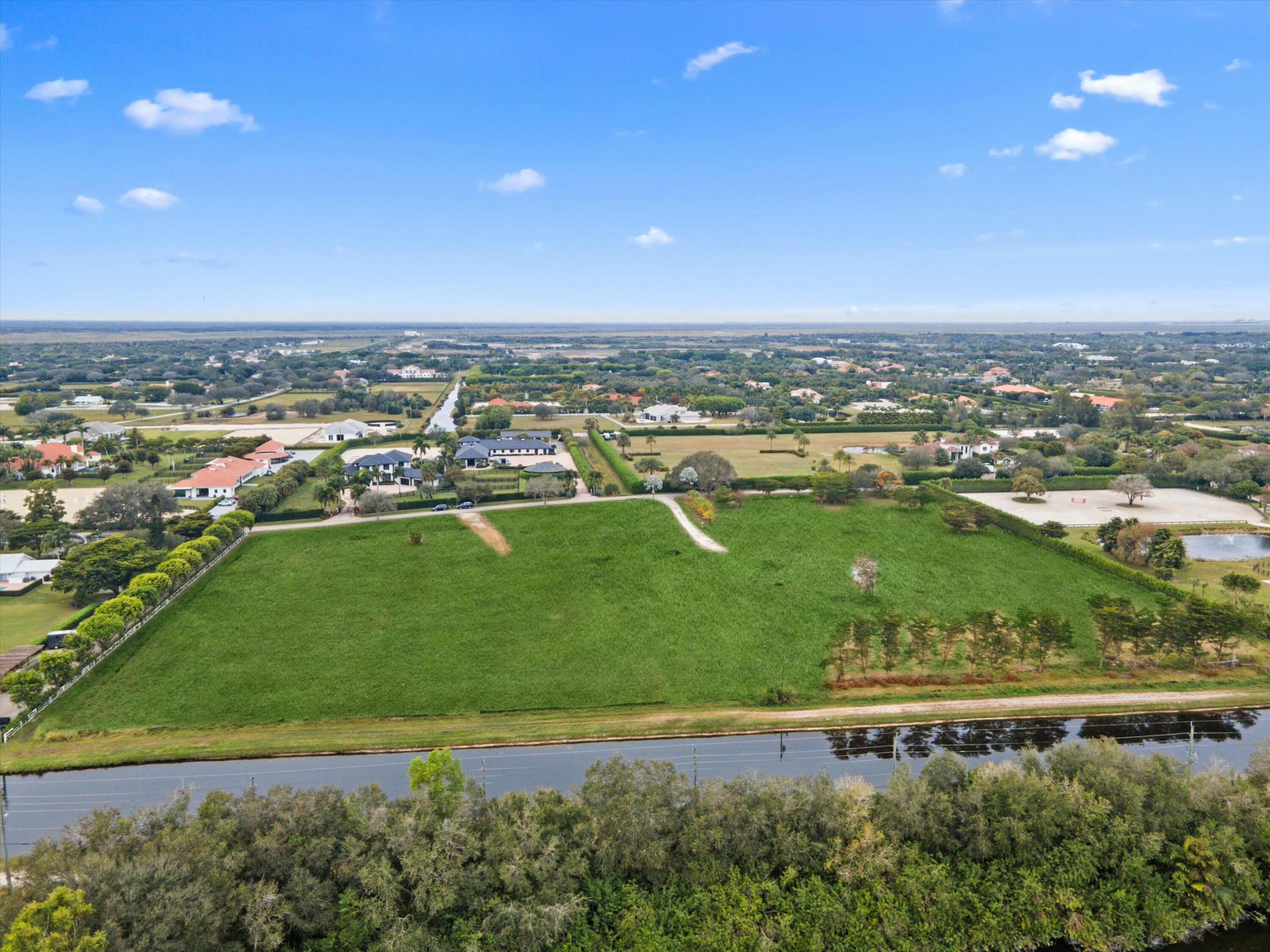Aerial view of a green field beside a canal, surrounded by homes and a riding arena.