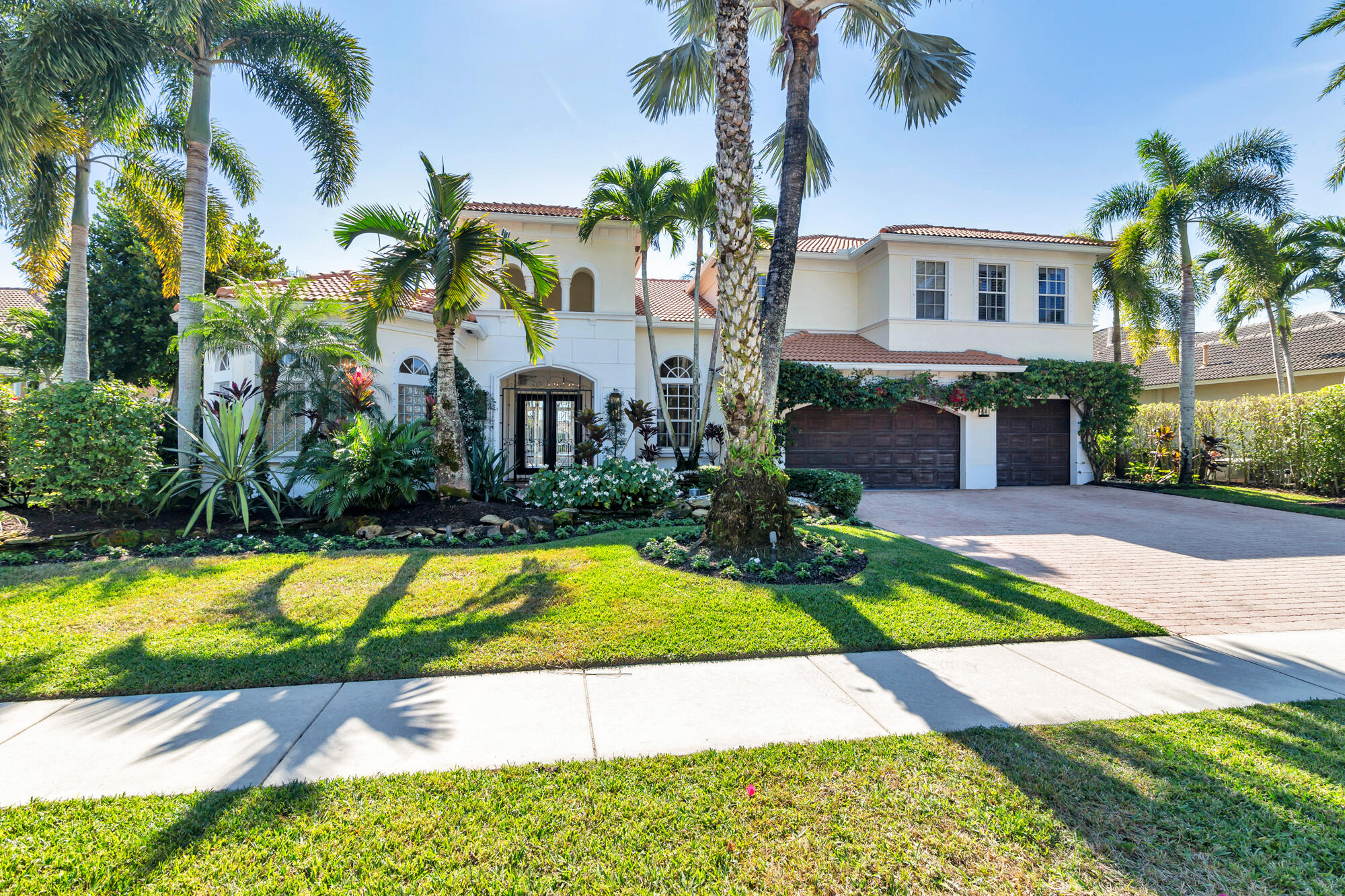 Two-story white home with a red tile roof, palm trees, tropical landscaping, and a three-car garage.