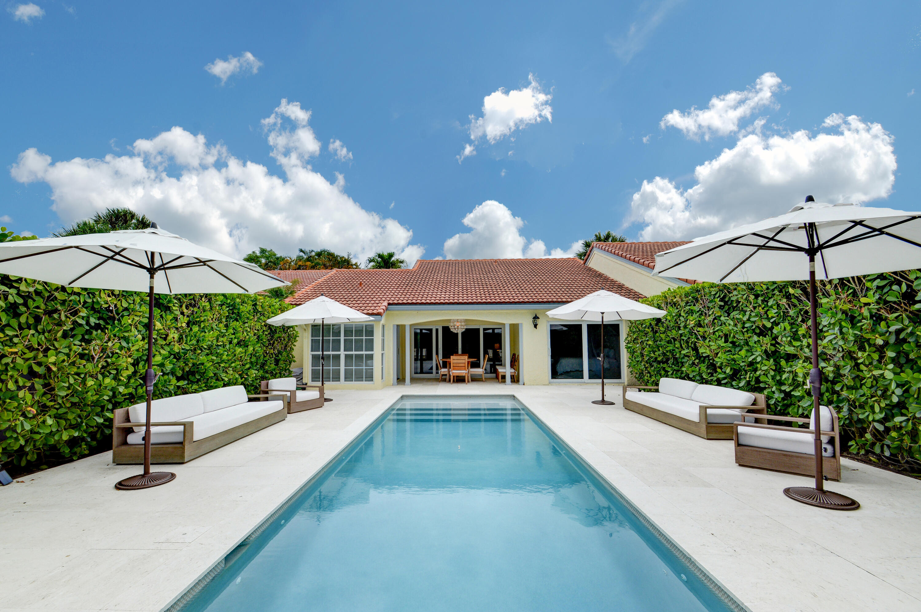 Backyard pool and patio with white umbrellas, lounge seating, and a single-story home.
