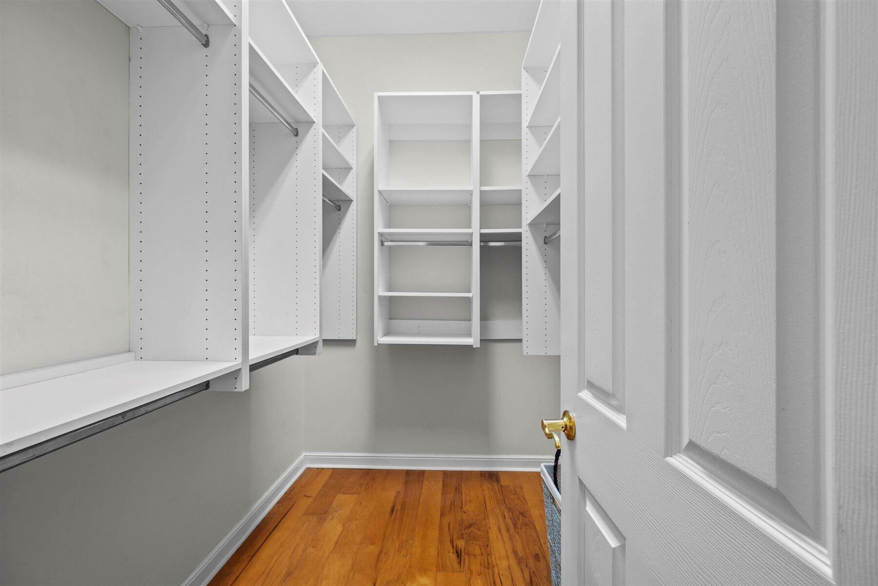 Walk-in closet with white built-in shelving, hanging rods, and hardwood flooring.