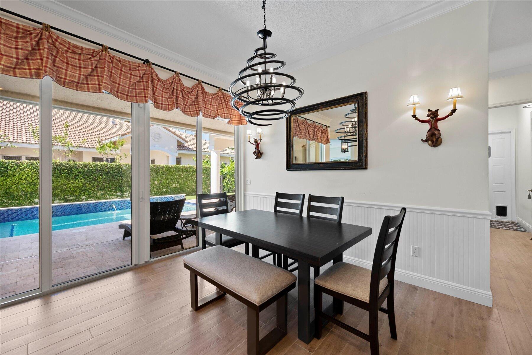 Dining room with a dark table and ring chandelier, overlooking a pool through sliding glass doors.