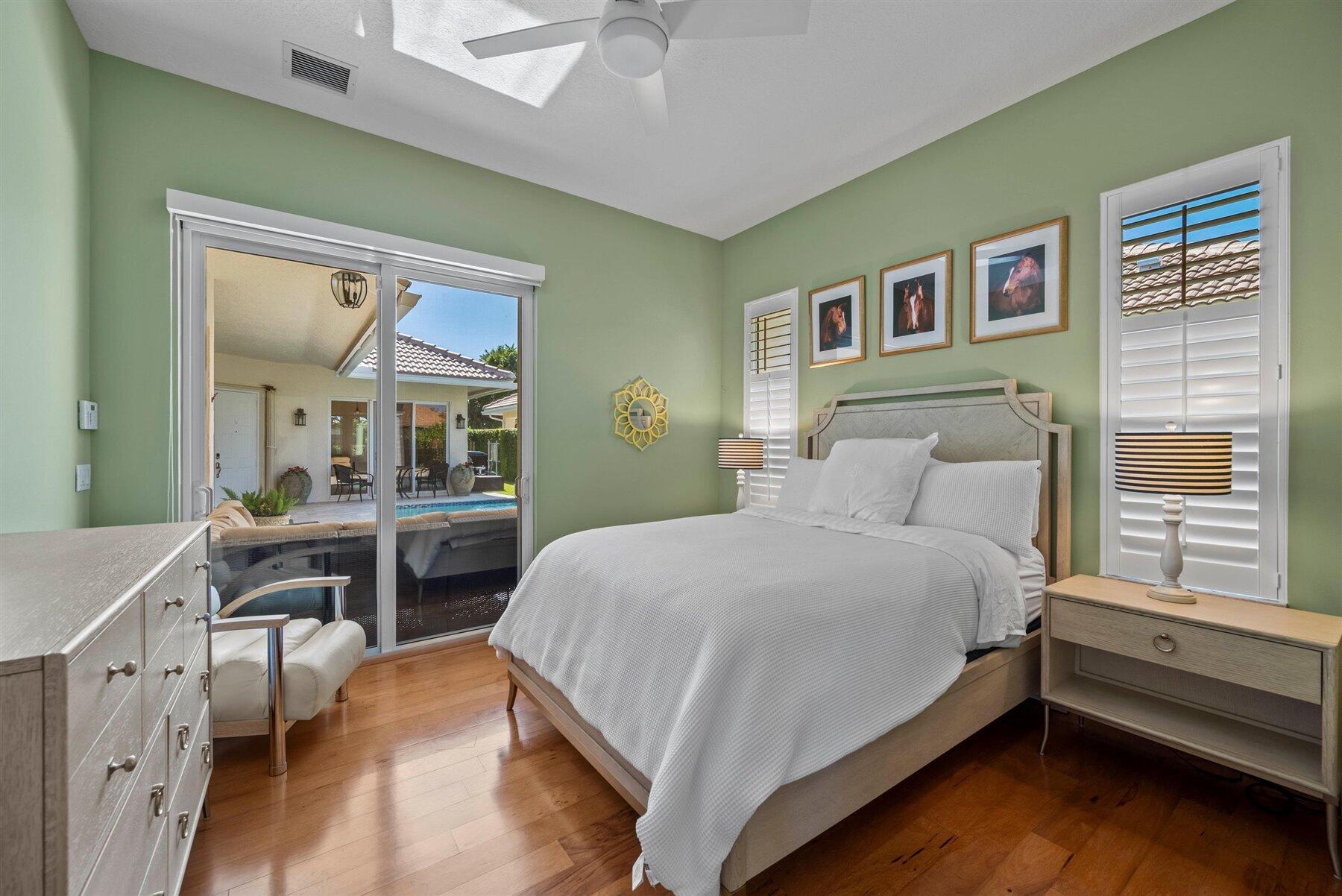Bedroom with sage green walls, a white bed, and sliding doors overlooking a pool.