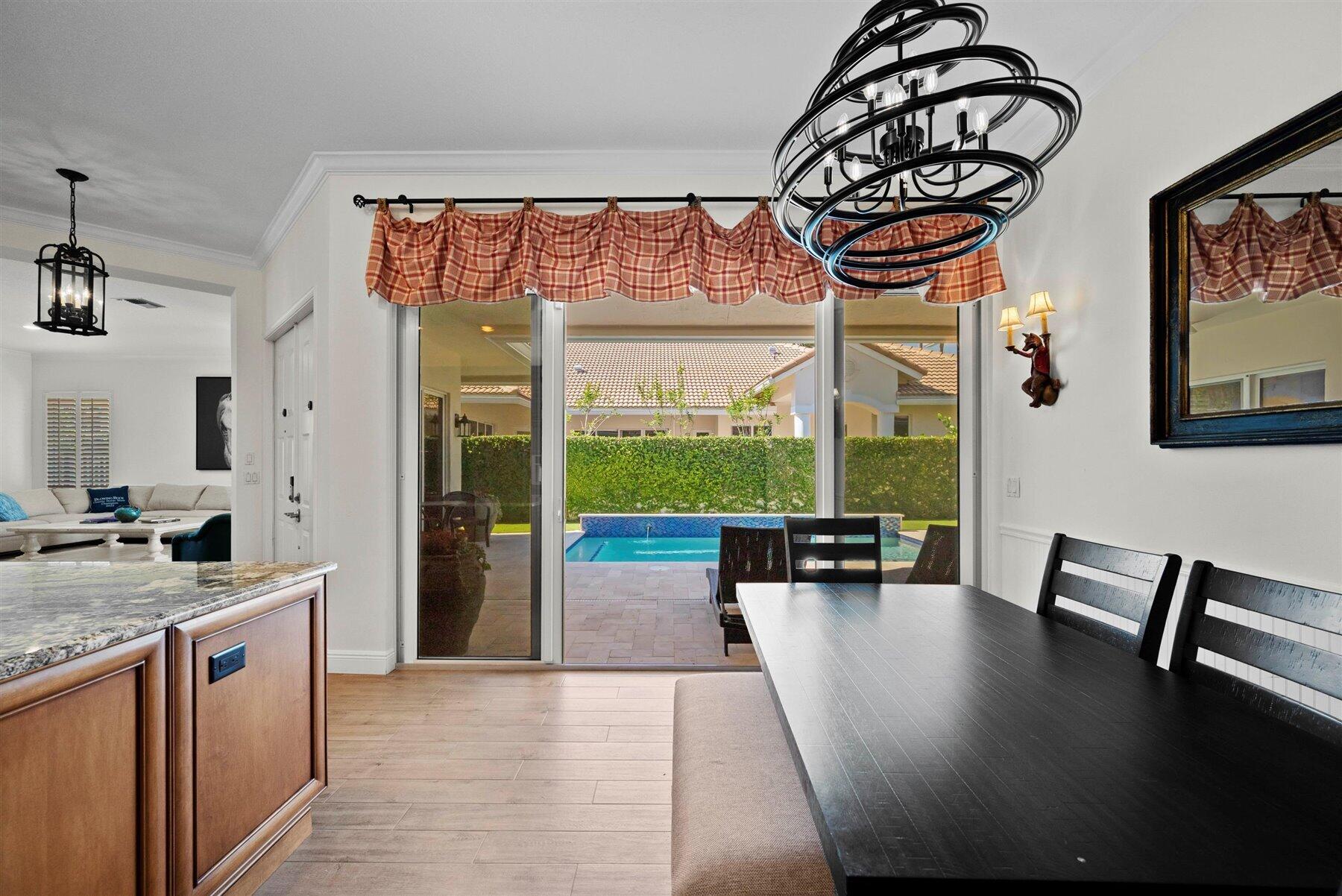 Dining room with a dark table and ring chandelier overlooking a backyard pool through sliding glass doors.