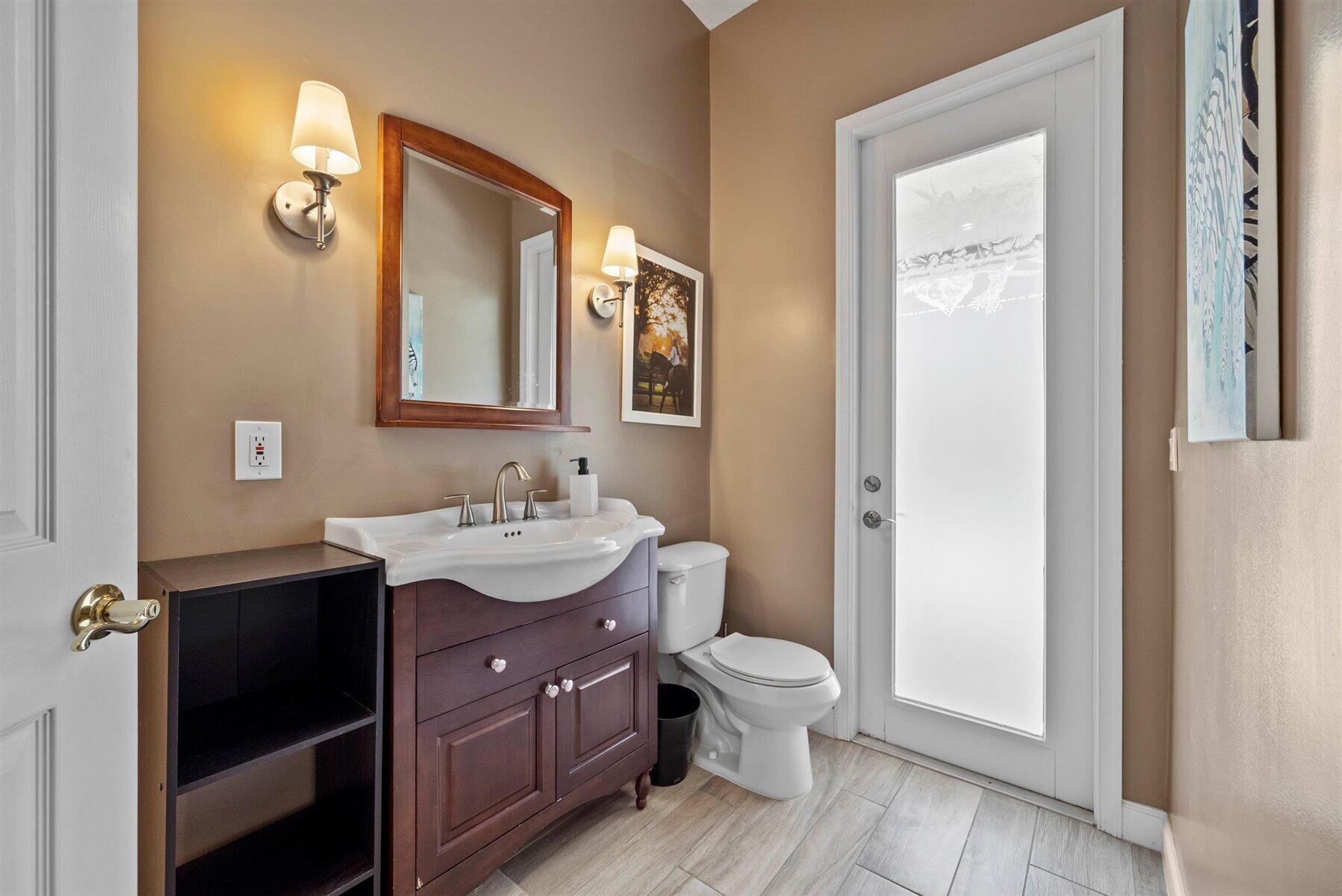 Bathroom with a dark wood vanity, white sink and toilet, and a tall frosted-glass door.